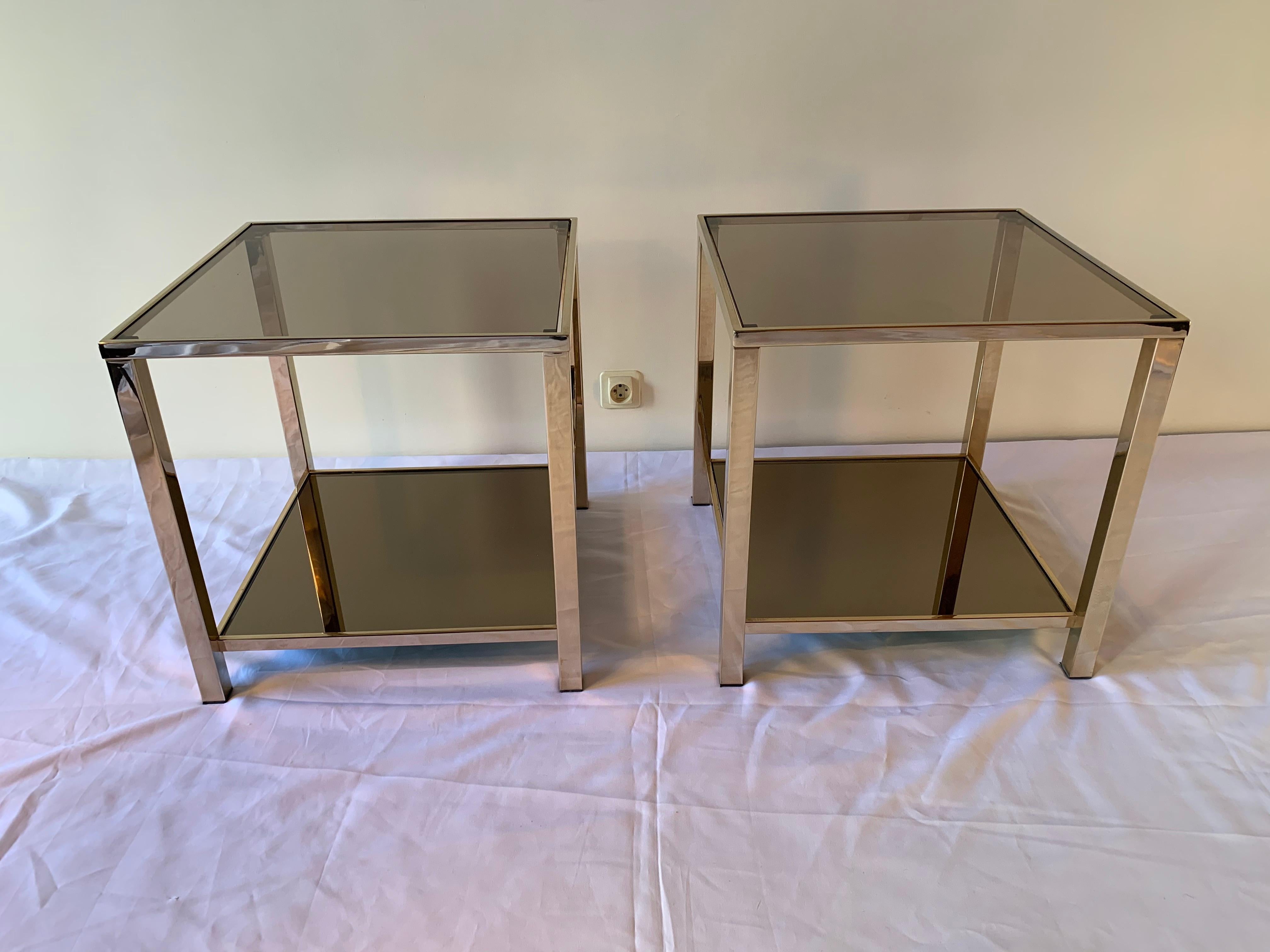 Beautiful pair of side tables with two levels designed and produced by Belgo Chrome, 1970s. The structure, gilded with 23-carat gold, showcases two trays. The top tray is made of smoked glass while the bottom tray is made of bronze mirror. The table