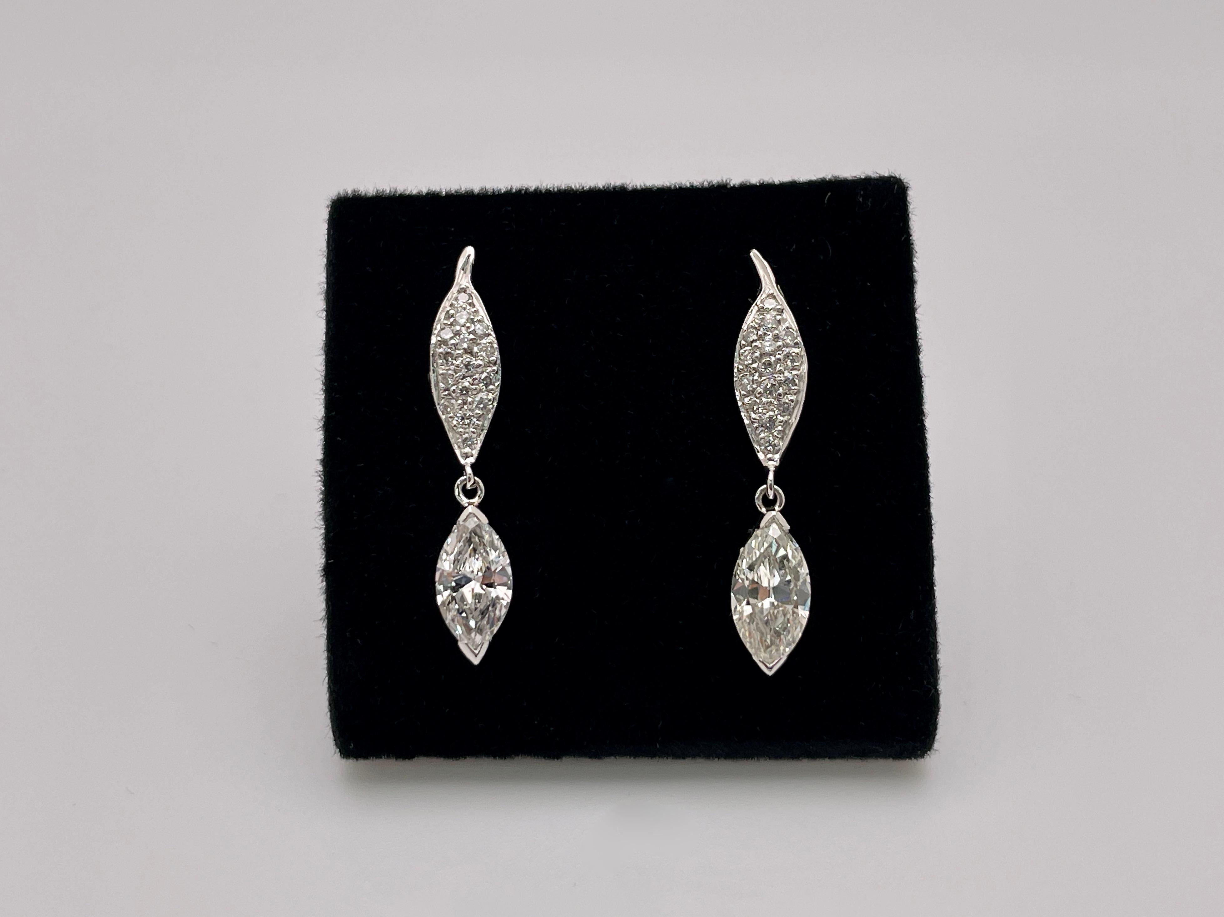 An original pair of platinum diamond drop dangle earrings. Each mounted with a marquise cut diamond weighing approximately 0.90 CT, one I color SI1 clarity, and the other J color SI1 clarity. Each accented with 14 small round cut diamonds in a