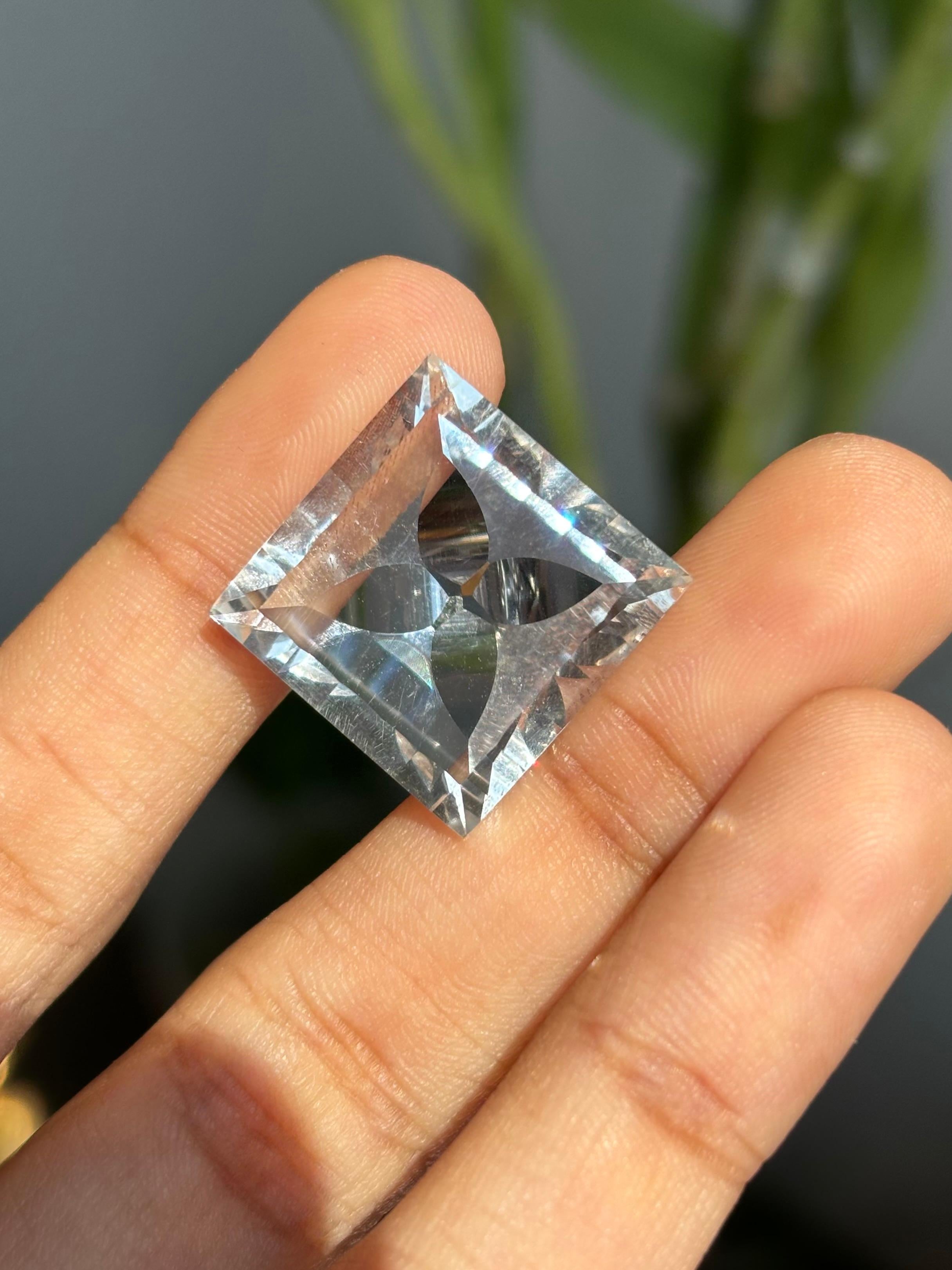 A stunning 23.03 Carat Topaz gemstone. It is completely natural and it is a clean stone.  The topaz stone is white in color. It is cut to perfection in a square shape, but the inside of the topaz resembles a flower-like shape, that is symmetrical