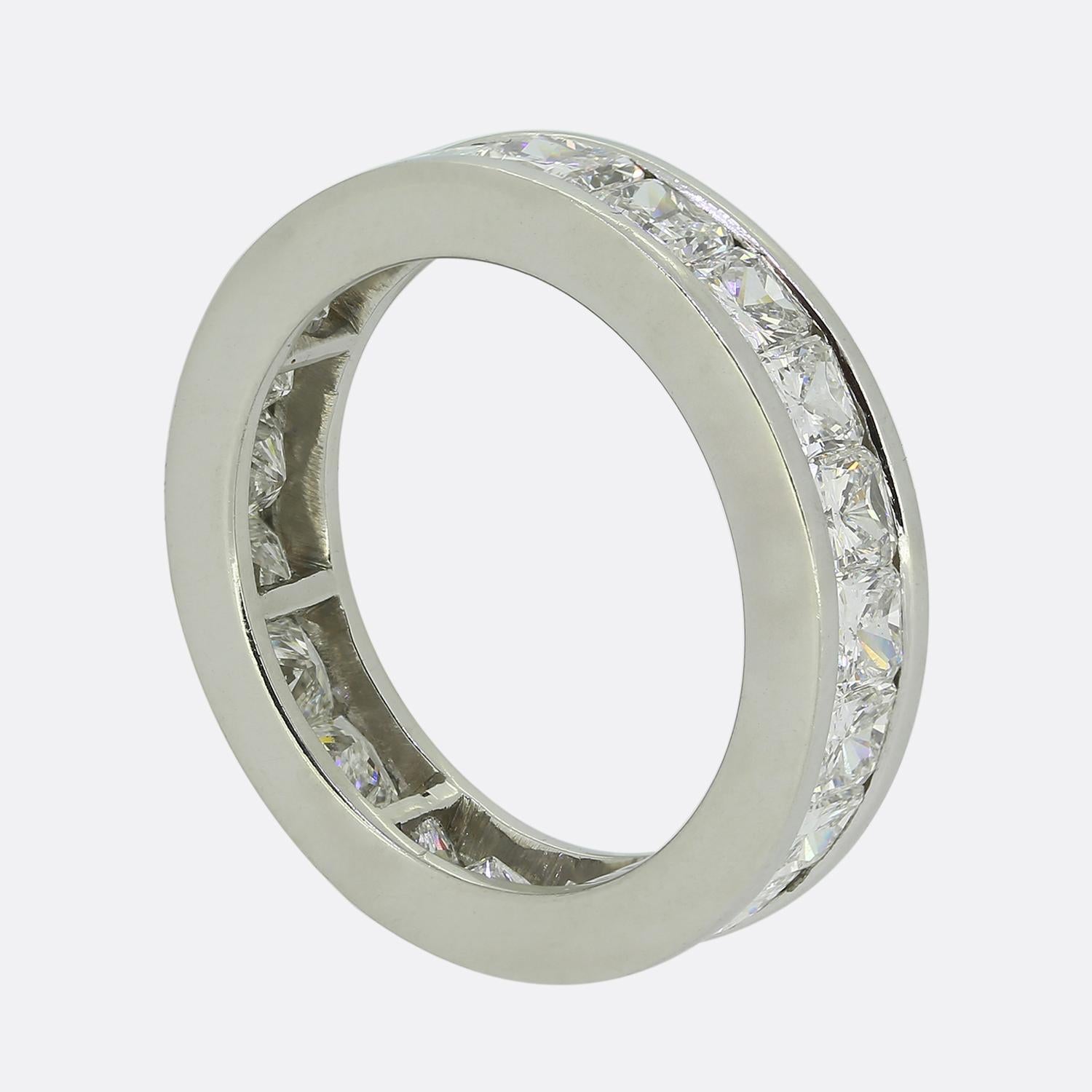 Here we have a classically styled diamond eternity ring. A plain polished platinum band is adorned with a continuous row of radiant-cut white diamonds, each set seamlessly within the channelled setting. The sleek design highlights the brilliance of