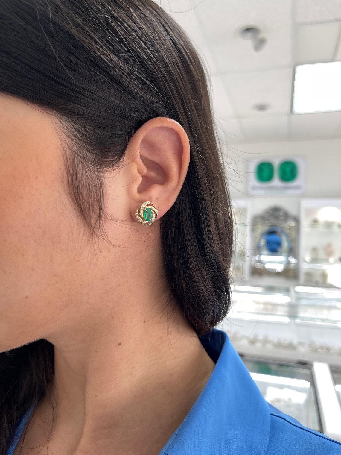 Elevate your elegance with our exquisite emerald and diamond stud earrings. Featuring 1.96-carats of alluring oval cut emeralds from the renowned origin of Zambia, their medium dark green hue and remarkable luster create a captivating allure.