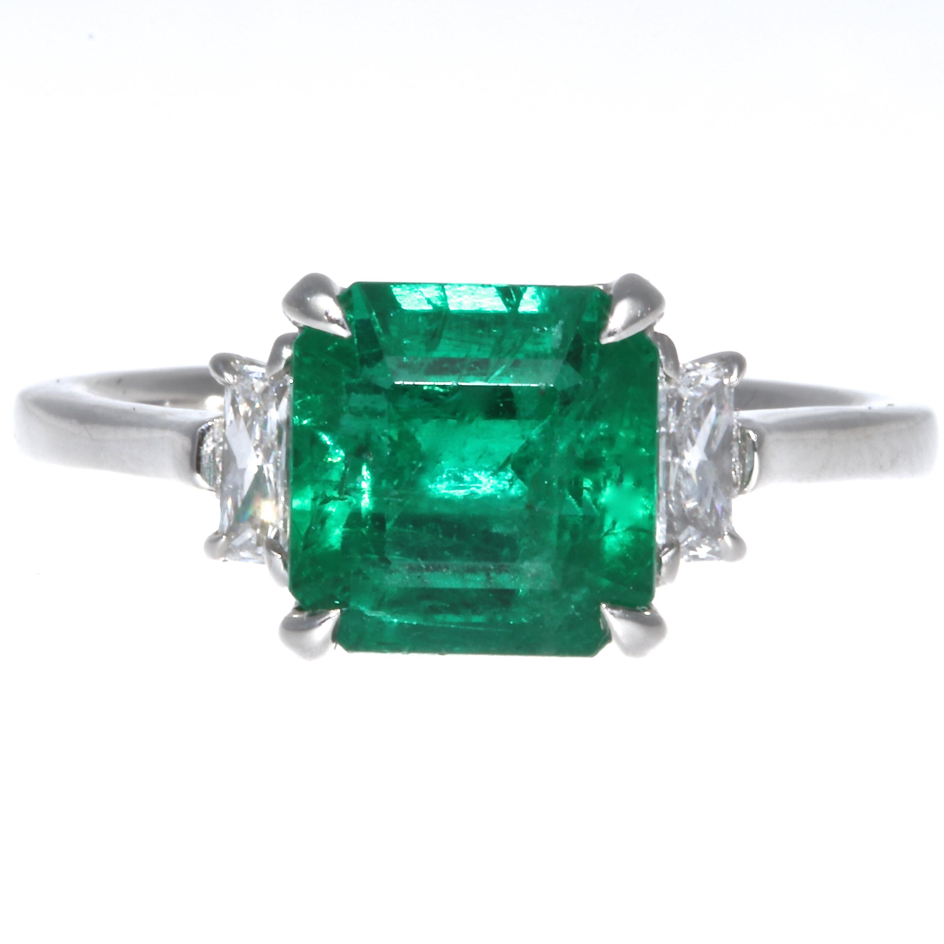 The richly colored  translucent Zambian emerald weighs 2.32 carats and is an excellent example of emeralds from that region. Set in a platinum ring, accented by 2 radiant cut diamonds  weighing approximately  0.20 carats,  H-I color VS clarity. Ring