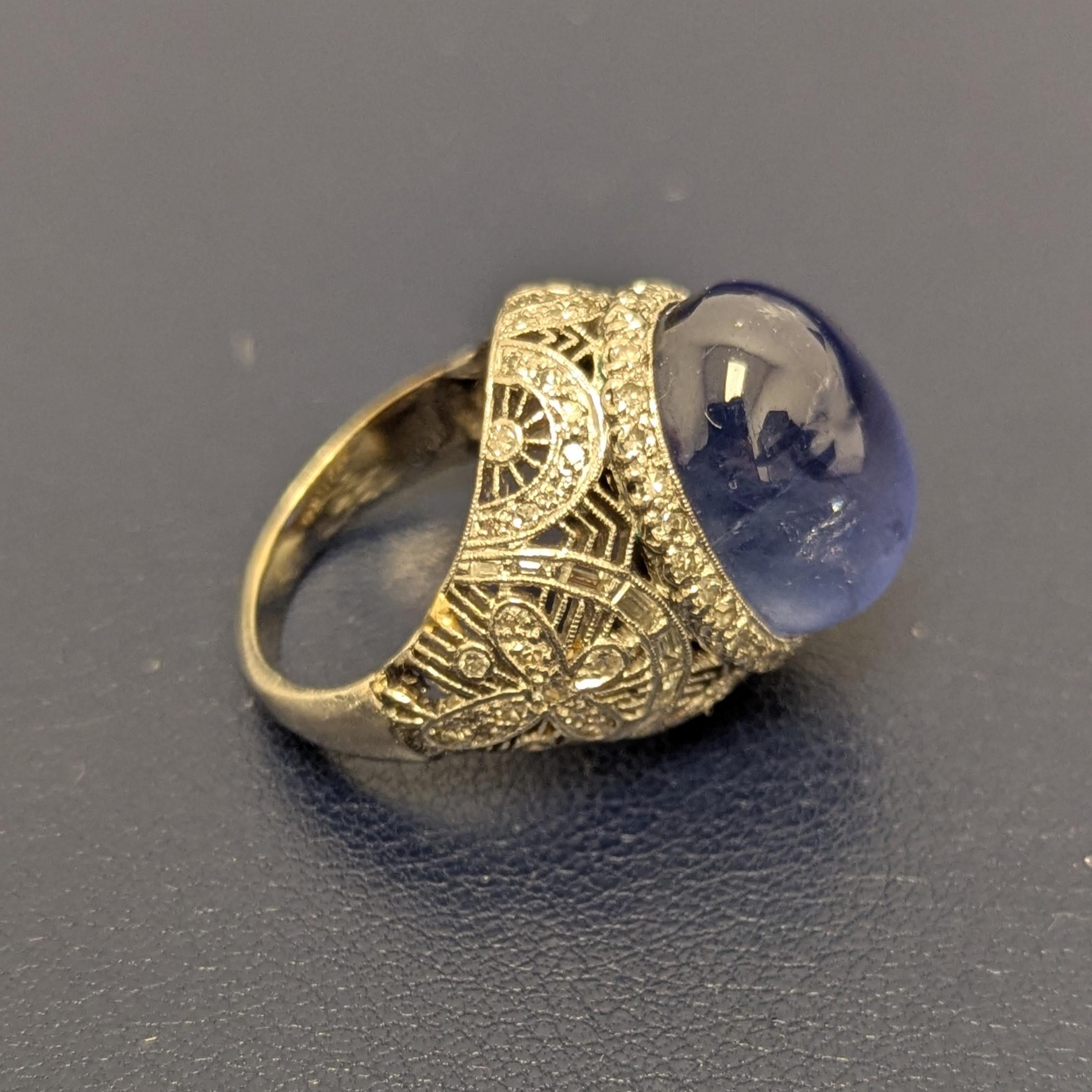 This ring features one centering oval star sapphire, which weighs approximately 23.25 carats, edged by single-cut diamonds, accented by curved bands of baguette diamonds, flanked by single-cut diamond flowers, all set on platinum filigree mounting.
