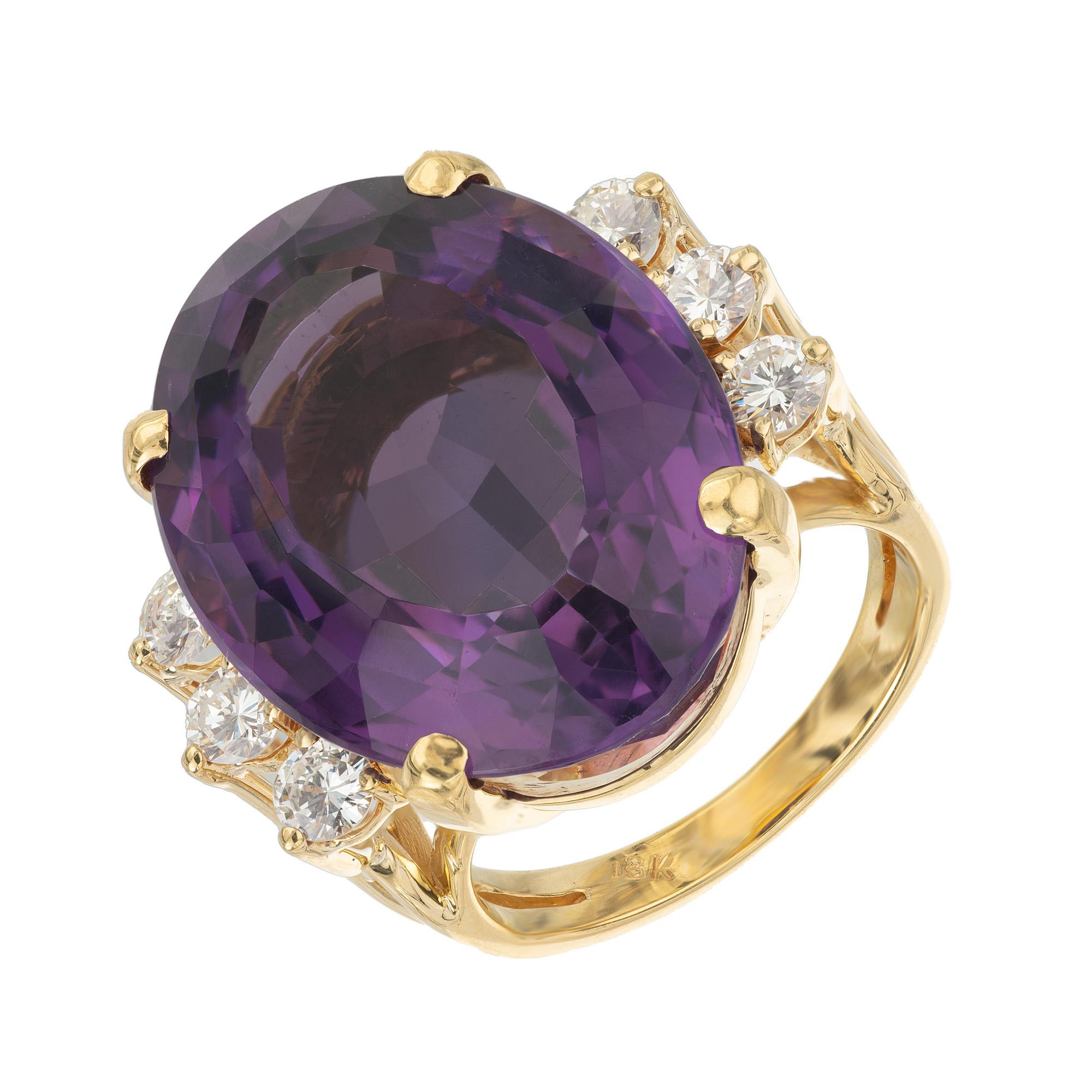 This 23.50ct oval Amethyst and Diamond yellow gold cocktail ring is a masterpiece of elegance. This magnificent Amethyst is a deep, rich purple, mounted in a 18k yellow gold setting. Surrounding this regal gemstone, are three round brilliant cut