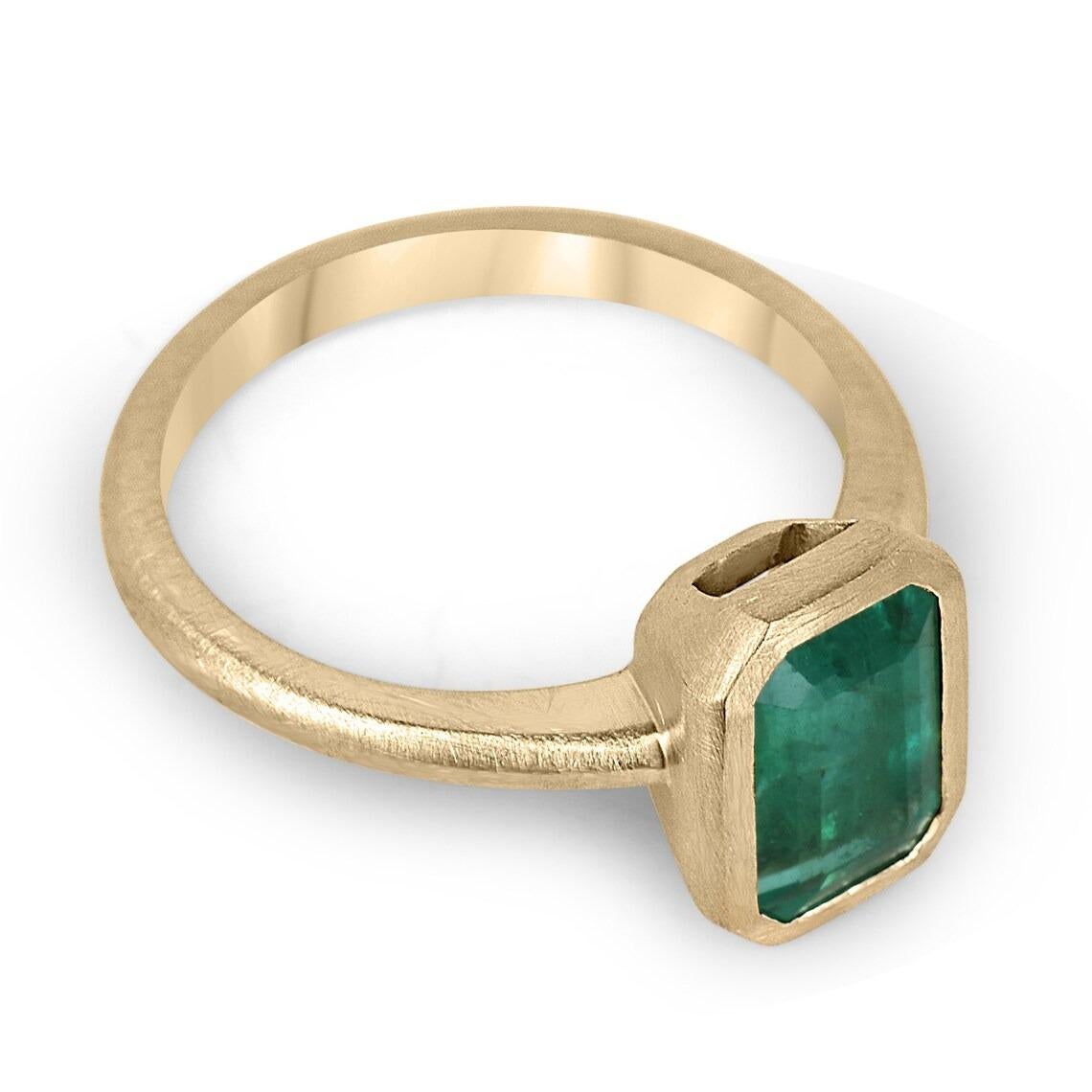 Displayed is a dark green emerald, solitaire, emerald-cut bezel ring in 14K yellow gold. This gorgeous solitaire ring carries a full 2.35-carat emerald in a sleek bezel setting. The emerald has incredible clarity and luster. This emerald has a great