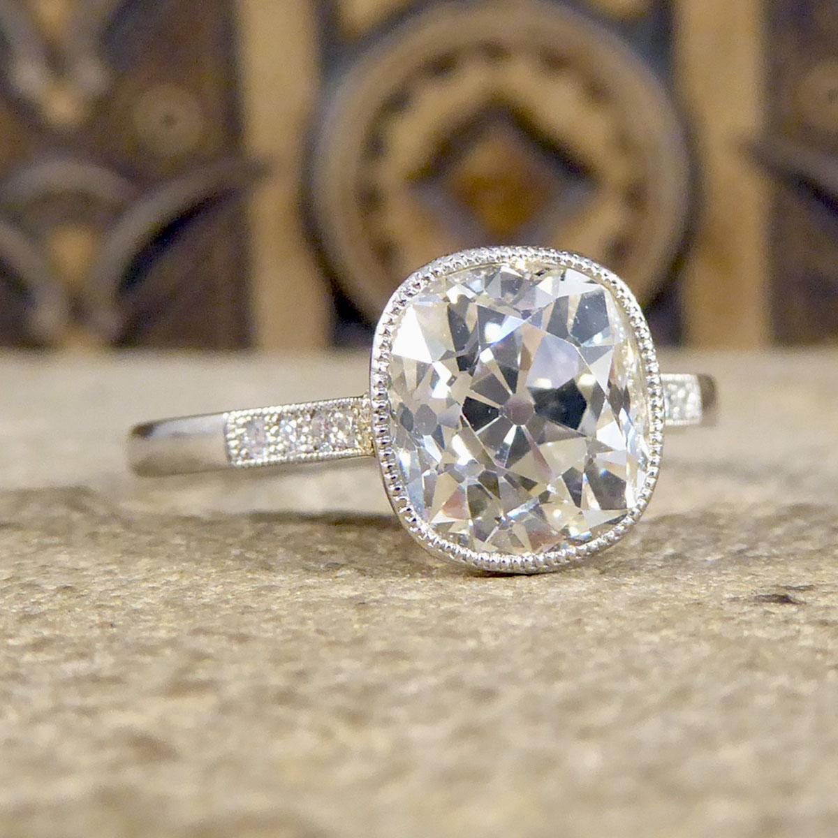 This beautifully sparkly engagement ring holds Old Cushion Cut Diamond weighing 2.35ct and is set in Platinum millegrain-edged rub over collar setting with a cut out Diamonds shaped wire gallery. A classic solitaire ring with an Edwardian style that