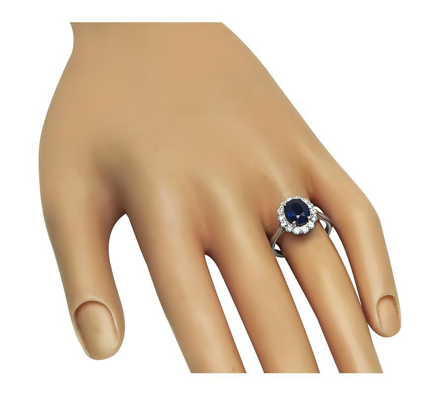Se trata de un elegante anillo de compromiso con halo de oro blanco de 18 quilates. El anillo está centrado con un precioso zafiro de talla ovalada que pesa aproximadamente 2.35 ct. El zafiro está acentuado por brillantes diamantes de talla redonda