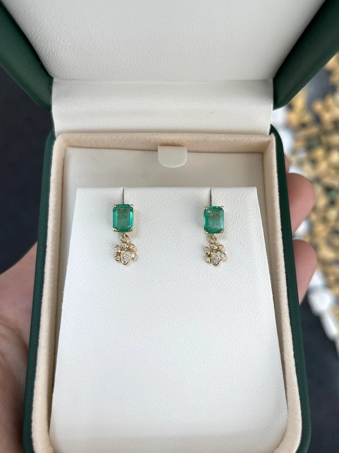 These stunning emerald earring studs boast 2.20 carats of emerald cut emeralds with a captivating lush green color, displaying very good luster and clarity. They are securely set in a four-prong basket, while below, diamond pave cluster paw prints