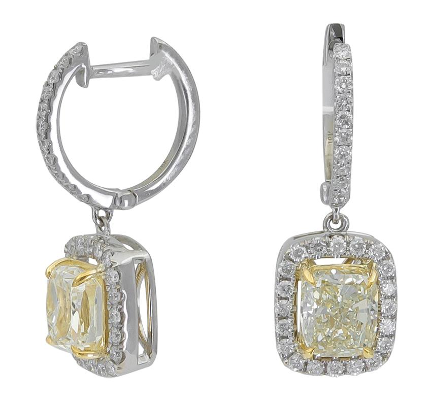 A simple and timeless pair of earrings perfect for everyday wear. Features two cushion cut yellow diamonds weighing 1.18 and 1.19 carats respectively, set in a floating halo accented with round brilliant diamonds. Suspended on a diamond hoop. Made