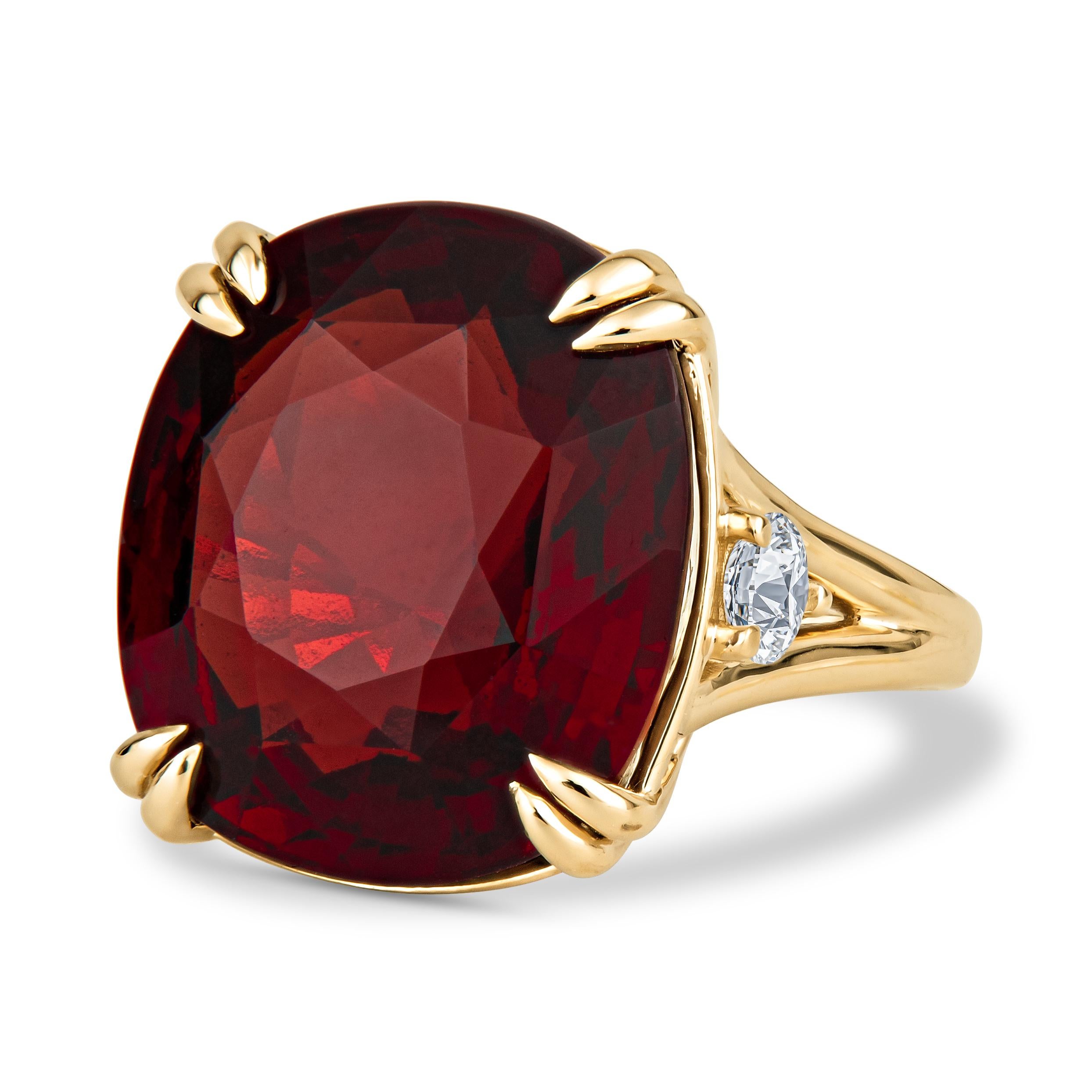 This exquisite ring features an extravagant 23.77ct deep red, cushion cut, spessartine garnet, accented by two 0.48ct total weight round brilliant diamonds. Spessartine garnet is one of the more rare varieties of garnet, especially in sizes this