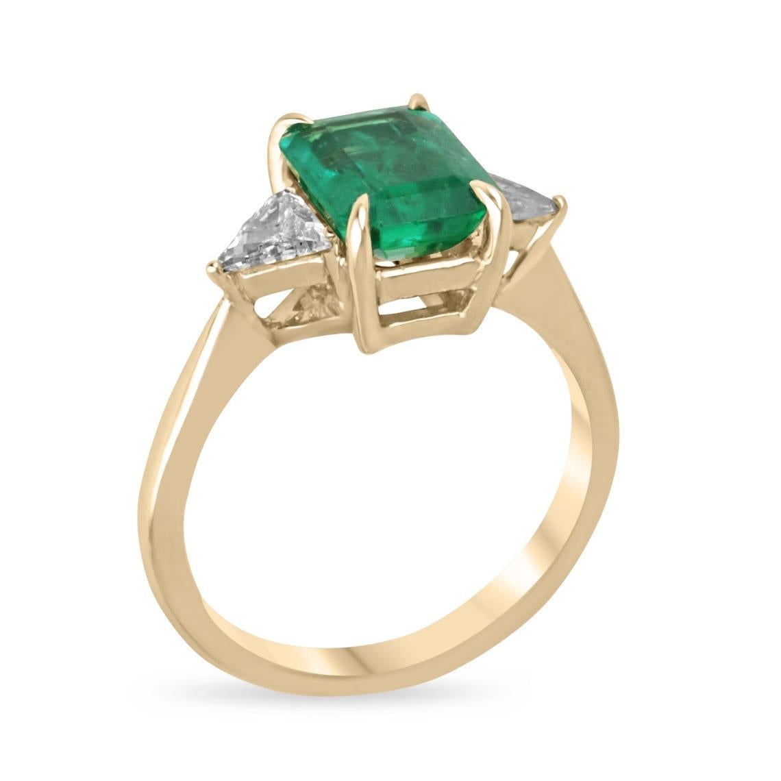 Dieser exquisite Ring mit drei Steinen zeigt einen lebhaften Smaragd im vertikalen Schliff, der einen fesselnden mittelgrünen Farbton mit halbtransparenter Klarheit aufweist. Flankiert von schillernden Diamanten im Billionenschliff in sicheren