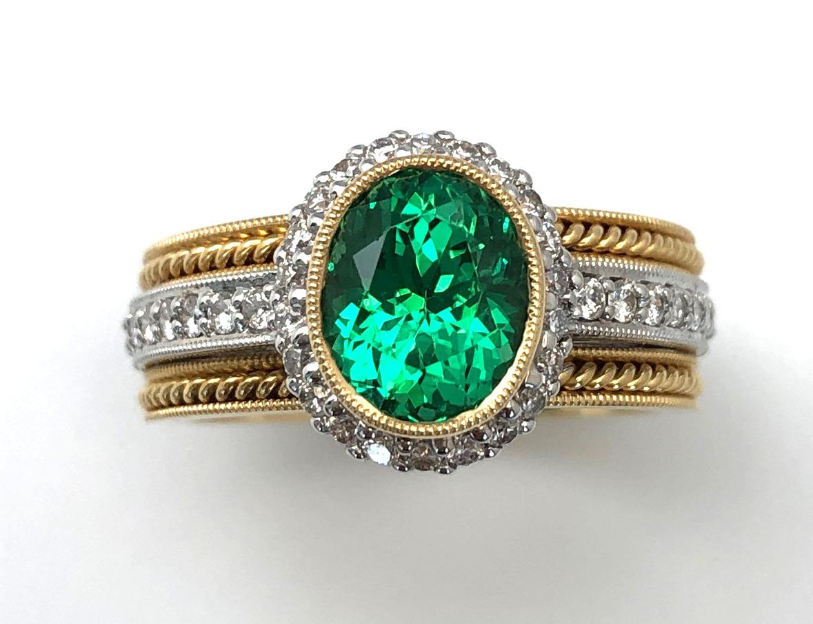 Tsavorite garnets capture the infinite beauty of spring in a single gemstone. This exquisite handmade ring features a vivid tsavorite green garnet surrounded by a halo of white diamonds set in luxurious 18k gold. The band includes brilliant diamonds