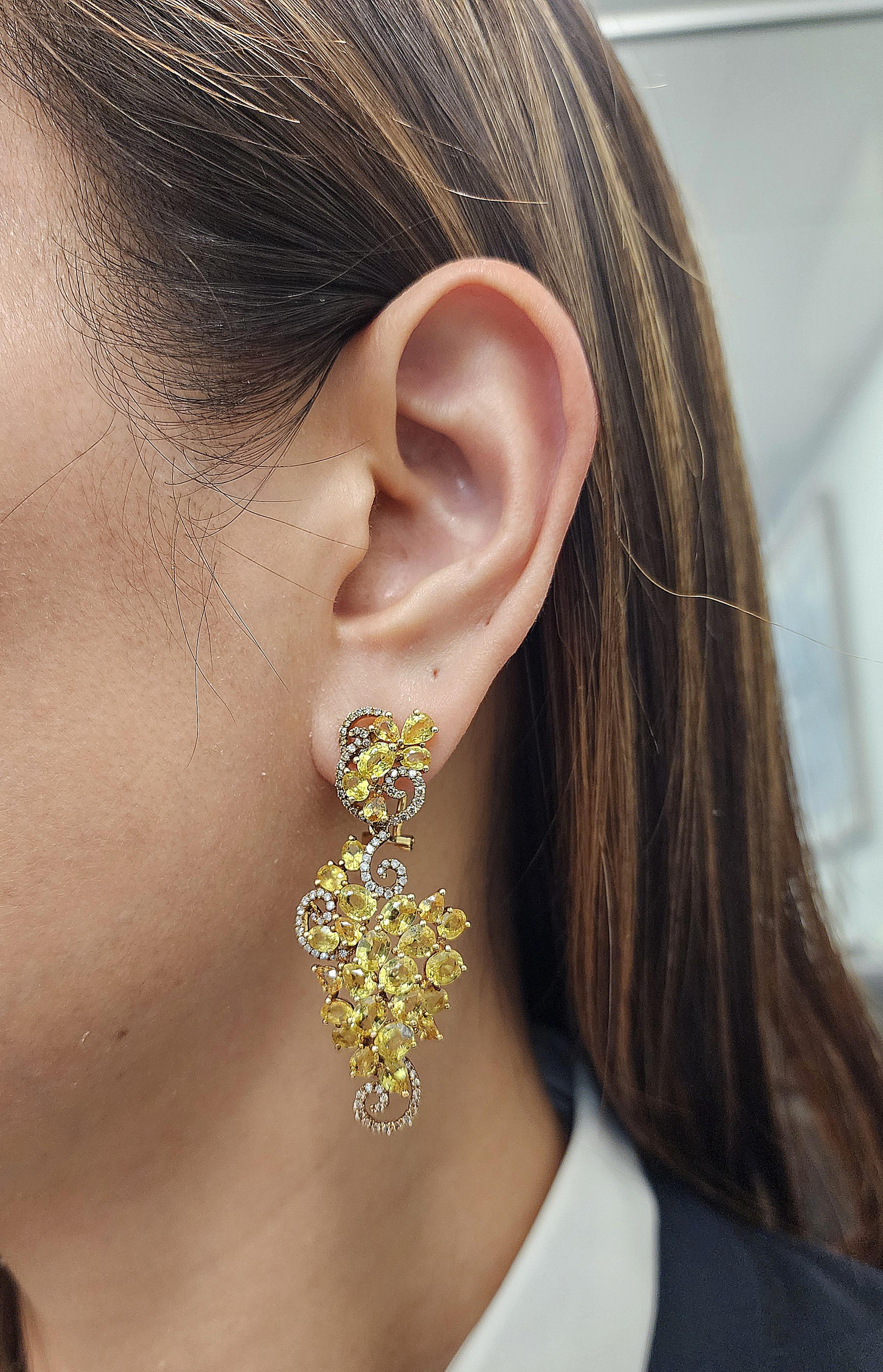  Discover the ultimate elegance and sophistication with these breathtaking 23.98 ctw natural yellow sapphire and diamond earrings. The vibrant yellow sapphires weigh a total of 22.80 carats. They are perfectly complemented by a halo of brilliant