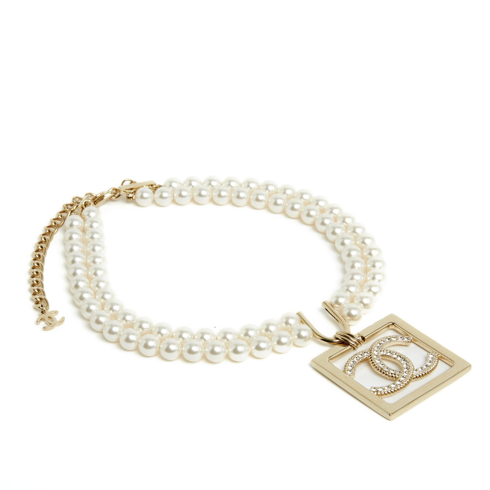 Ensemble Chanel, collection SS2023, composé d'un collier ras de cou à 2 rangs de perle fantaisie blanche, motif central en métal doré avec pendentif carré orné d'un logo CC incrusté de strass blancs, s'attachant par un mousqueton sur une chaîne en