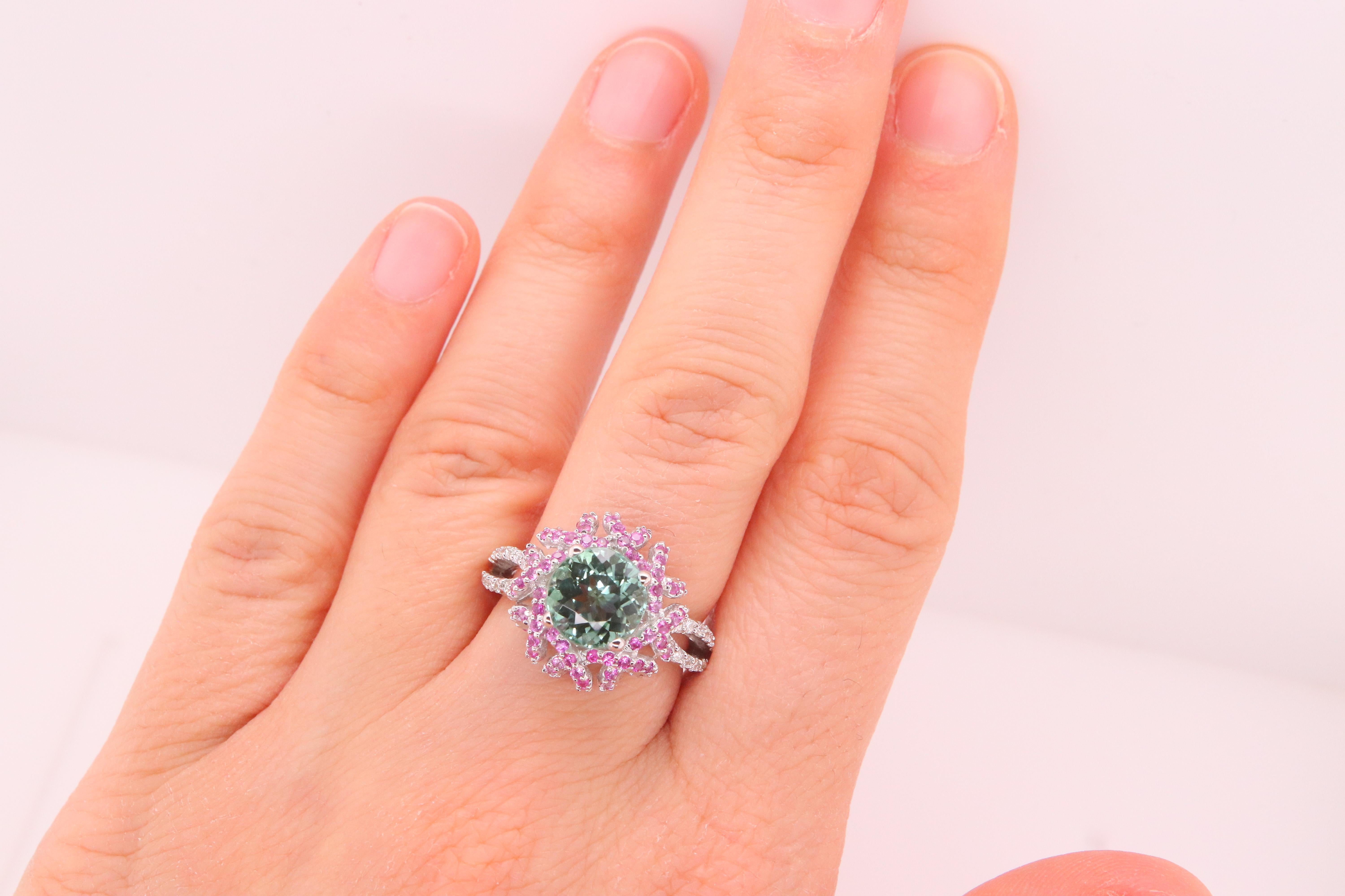 Material: 18K White Gold 
Center Stone Details: 1 Round Green Tourmaline at 2.4 Carats - 8mm
Mounting Stone Details: 96 Round Pink Sapphires at 0.70 Carats
Diamond Details: 24 Brilliant Round White Diamonds at Approximately 0.20 Carats - Clarity: SI