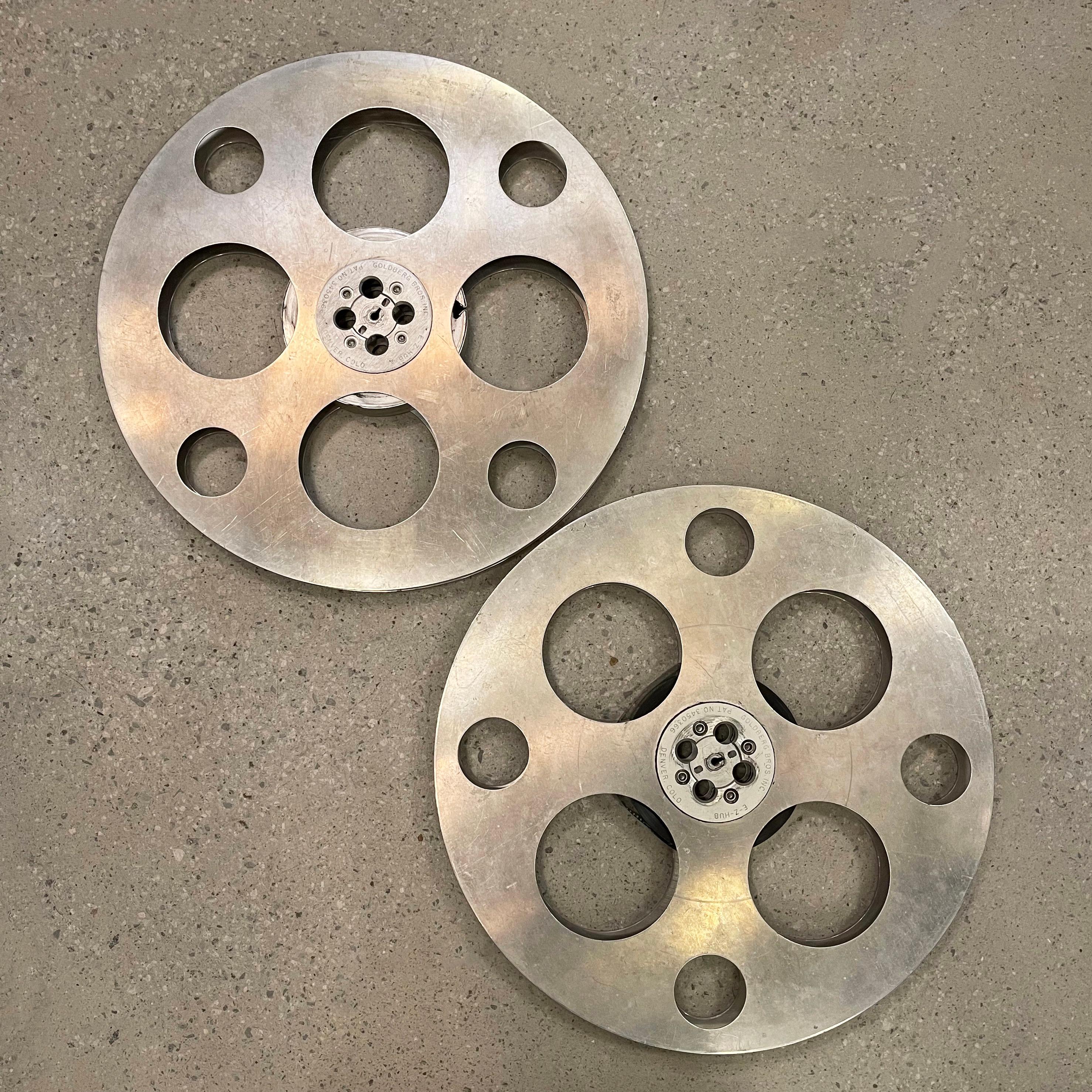 Large, 24 inch diameter, industrial, midcentury, film reels by Goldberg Brothers are great accent pieces or wall hangings. Both are clean on one side and have their original markings on the other  side. One reel still has film wound inside. Sold
