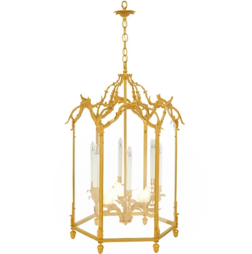 Questa eccezionale lanterna a sei lati, realizzata in stile Luigi XV, esemplifica l'eleganza e la maestria delle arti decorative francesi del XIX secolo. Meticolosamente costruita in ottone finemente cesellato e sontuosamente placcata in oro a 24