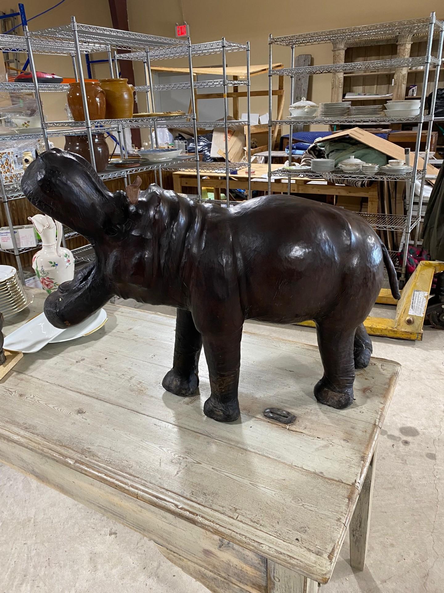 Una gran escultura de hipopótamo de cuero marrón oscuro, realista en los detalles y con la boca muy abierta. La escultura tiene un acabado envejecido y desgastado, que le da un aspecto rústico. Hecha a mano en Inglaterra, esta reproducción envuelta