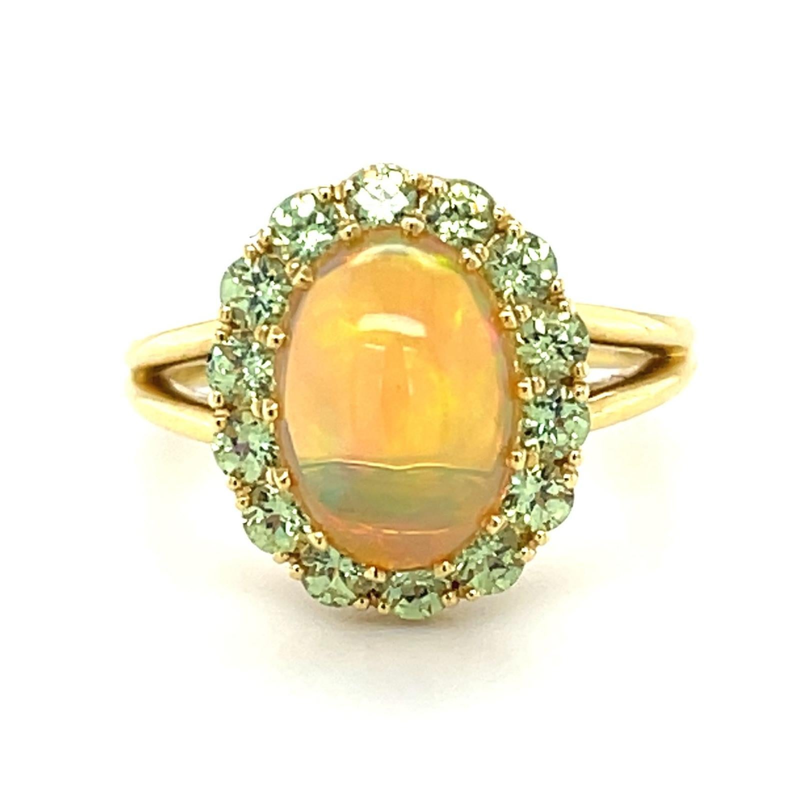 This stunning cocktail ring features a beautifully high-domed opal set in 18k yellow gold and framed with sparkling round Tsavorite green garnets! The opal is a 2.40 carat gem with gorgeous play-of-color, and the greens in the center gem come to