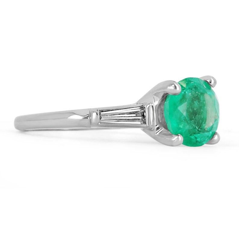 A classic among engagement rings, this genuine emerald, and tapered diamond engagement ring features a vibrant round Colombian emerald. The genuine rare gemstone has an incredibly deep bluish-green color and excellent eye clarity. The gem sits