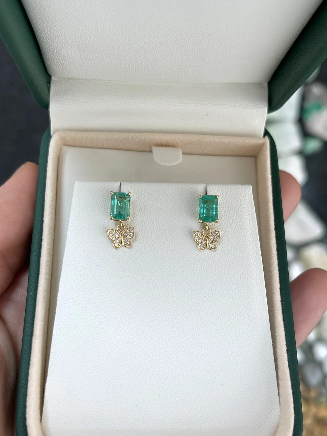 These exquisite dangle earrings feature stunning emerald-cut emeralds, elegantly set in a north-to-south orientation. The emeralds exhibit a mesmerizing medium-dark green hue, with good luster and clarity. Adorned with delicate butterfly motifs of