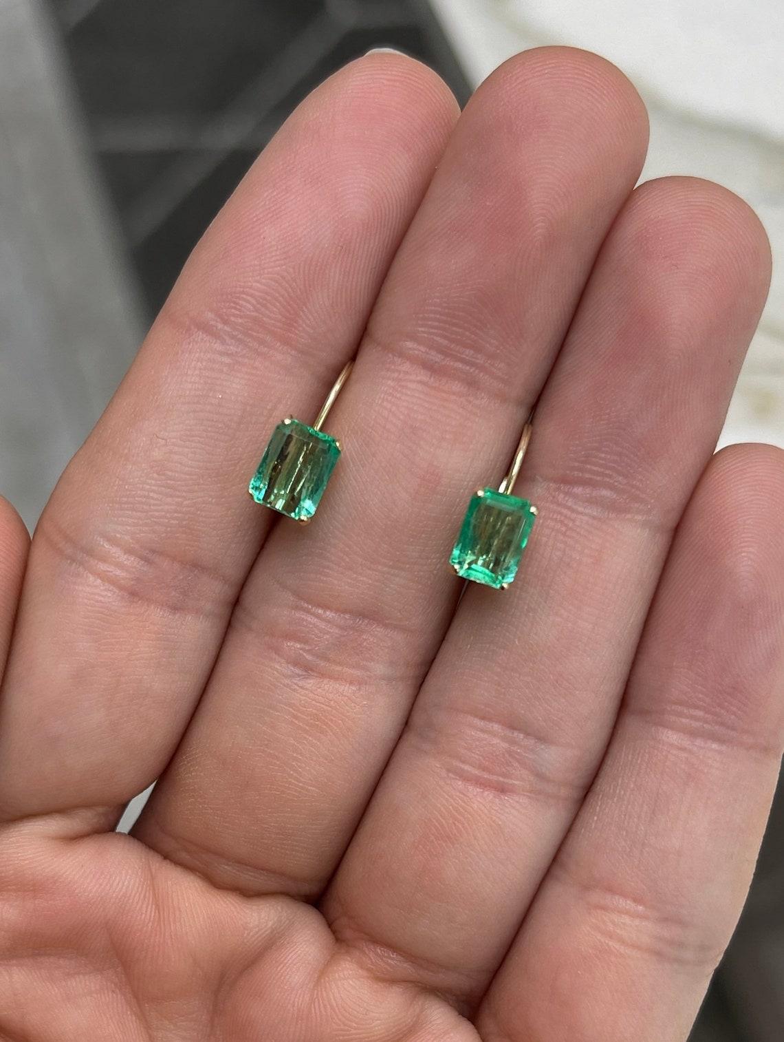 A simple pair of emerald cut-emerald lever back earrings made in 14K yellow gold. The chic pair of lever back earrings feature green, natural Emeralds. The emeralds have beautiful eye clarity, displaying minor flaws that are normal in all