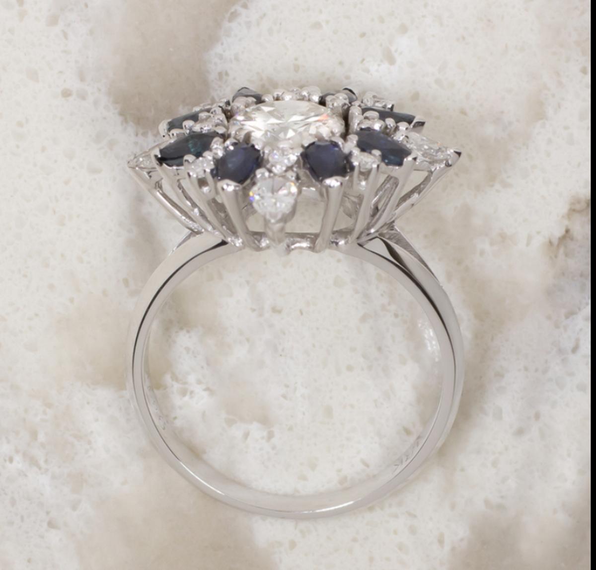 This high quality, gorgeous, and eye catching vintage ring features a substantial 1.12 carat round brilliant cut diamond set in the middle of a brightly glittering halo of dazzling diamonds and rich blue sapphires! Measuring a substantial 20.2mm