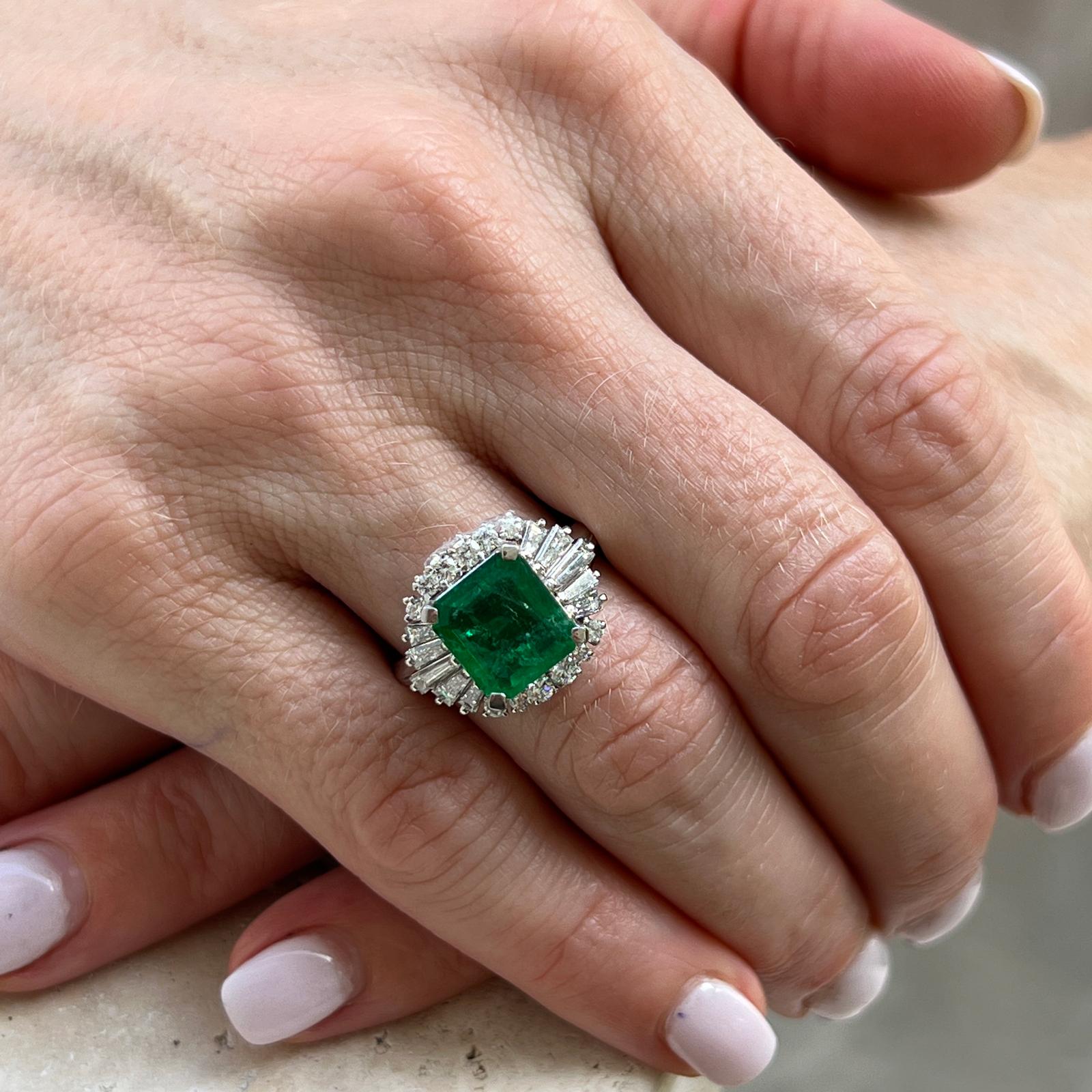 Beautiful emerald diamond cocktail ring crafted in platinum. The ring features a 2.45 carat natural green emerald cut emerald in a ballerina setting. The round and baguette cut diamonds weigh .94 carat total weight and are graded G-H color and VS