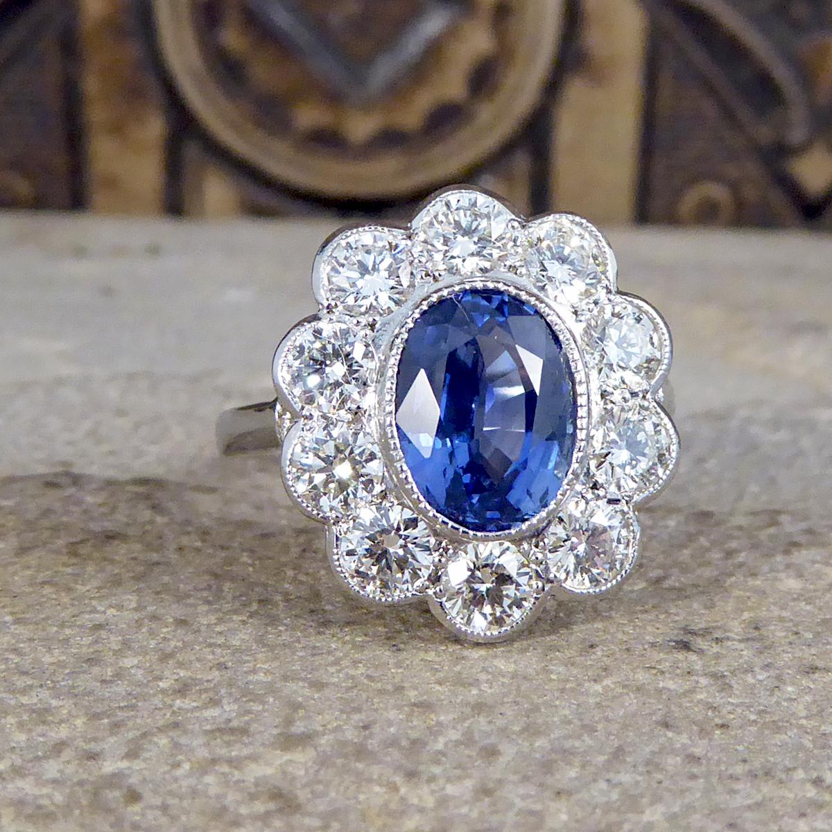 This contemporary ring holds a 2.45ct dazzling blue Sapphire in the centre of the ring and surrounded by 10 Modern Brilliant cut bright and clear Diamonds making a cluster. Complimenting the Sapphire gemstone is a Platinum rub over collar setting,