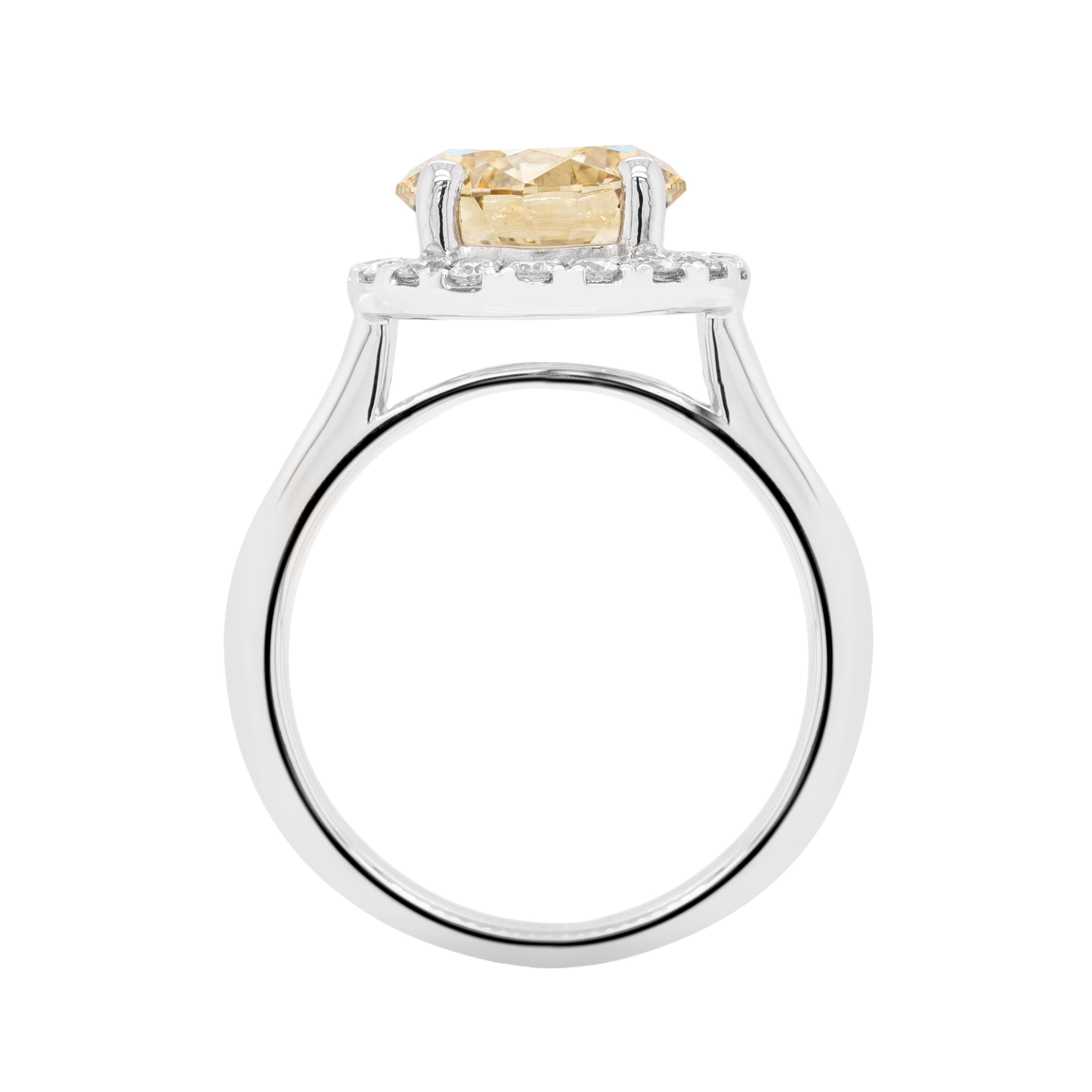 This stunning engagement ring features an impressive round brilliant cut fancy champagne colour diamond weighing 2.46ct, mounted in a four claw, open back setting. The wonderful stone is surrounded by a halo of 18 fine quality round brilliant cut