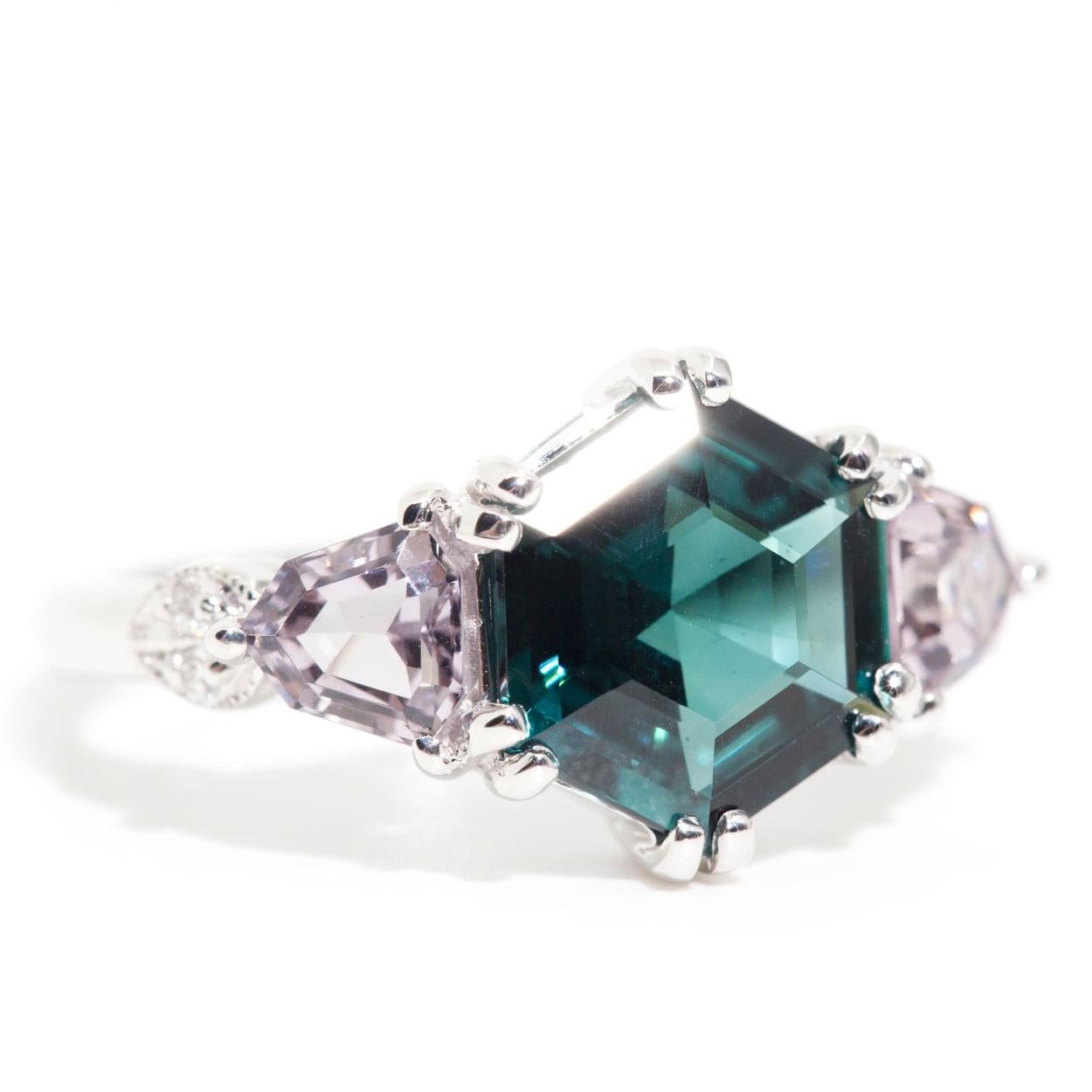 Forged in 18 carat white gold is this contemporary ring featuring a striking 2.46 carat hexagon cut bright deep teal tourmaline flanked with two bright pale purple shield cut Spinels, finished with sparkling round brilliant diamonds. We have named