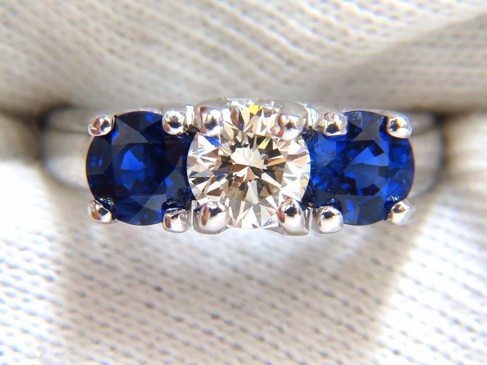 Diamant classique et saphirs, trois pierres

.80ct. Diamant de taille ronde

Full Cut Brilliant

J-color Vs-2 Clarity

5.8mm



Saphirs bleus naturels ronds sur le côté : 1.68ct. 

Bleu royal vibrant et transparent

Full cut et Full