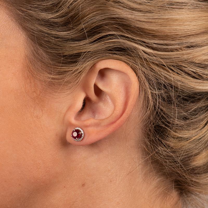 These stud earrings feature 2.48 carat total weight in natural round rubies accented by a halo of 0.18 carat total weight in diamonds set in 18 karat white gold. Friction post with butterfly back. 
Measurements: Approximately 8.6mm in circumference