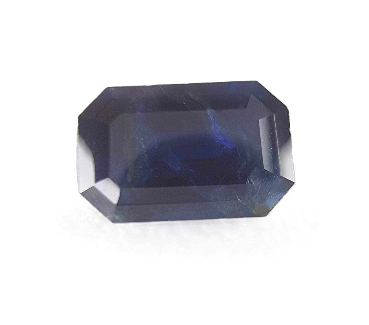 This 2.40-carat natural sapphire presents a deep, almost inky blue hue, with a rectangular cut that enhances its structured elegance. Measuring approximately 6.8 mm by 3.9 mm, the gem features beveled corners that create crisp, angular reflections,