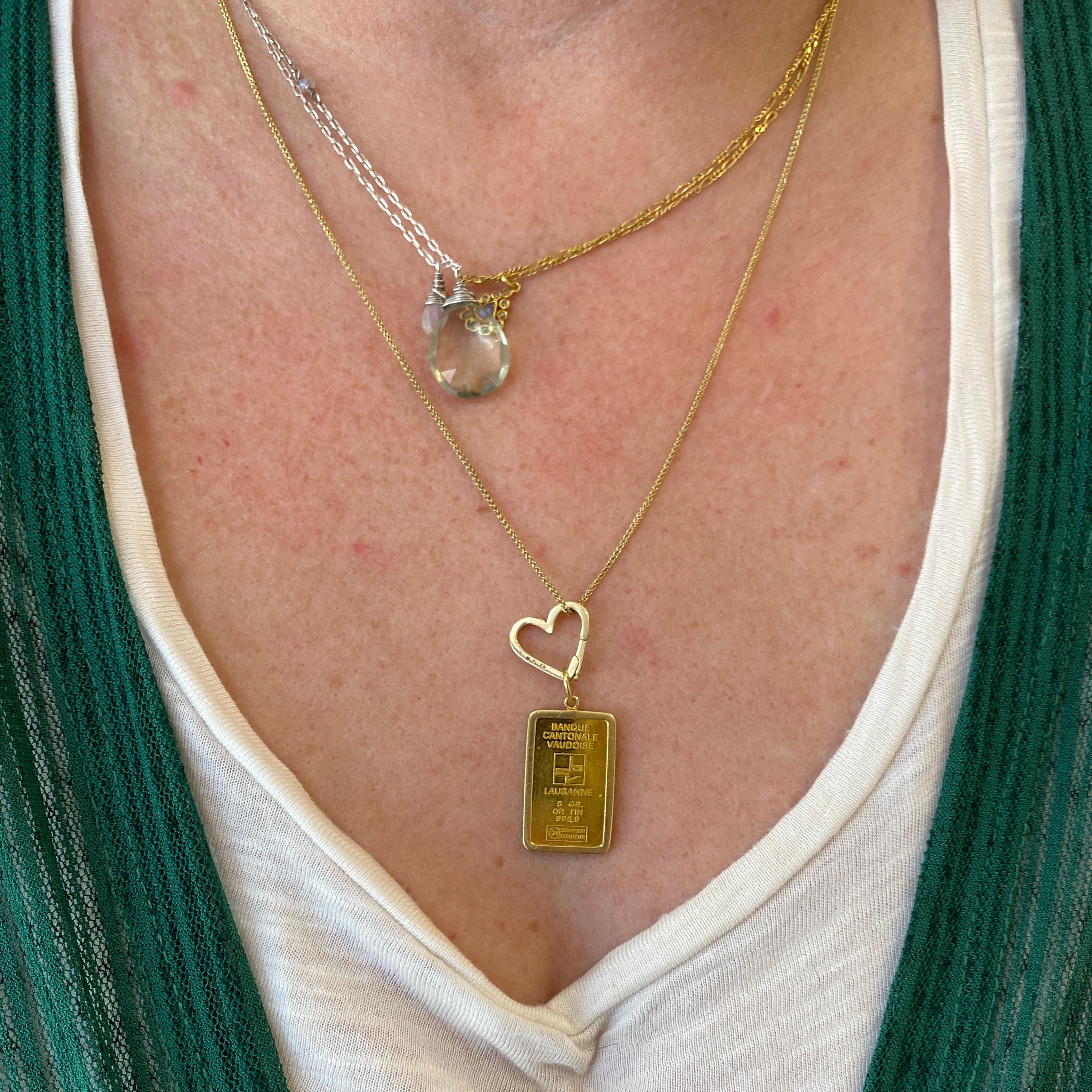 ¡Este colgante bellamente conservado está listo para ser amado de nuevo! Un lingote de oro de 24k de 5 g se asienta en un marco de oro amarillo de 14k de líneas limpias, listo para llevar en una cadena de hasta 4 mm de ancho. El lingote procede del