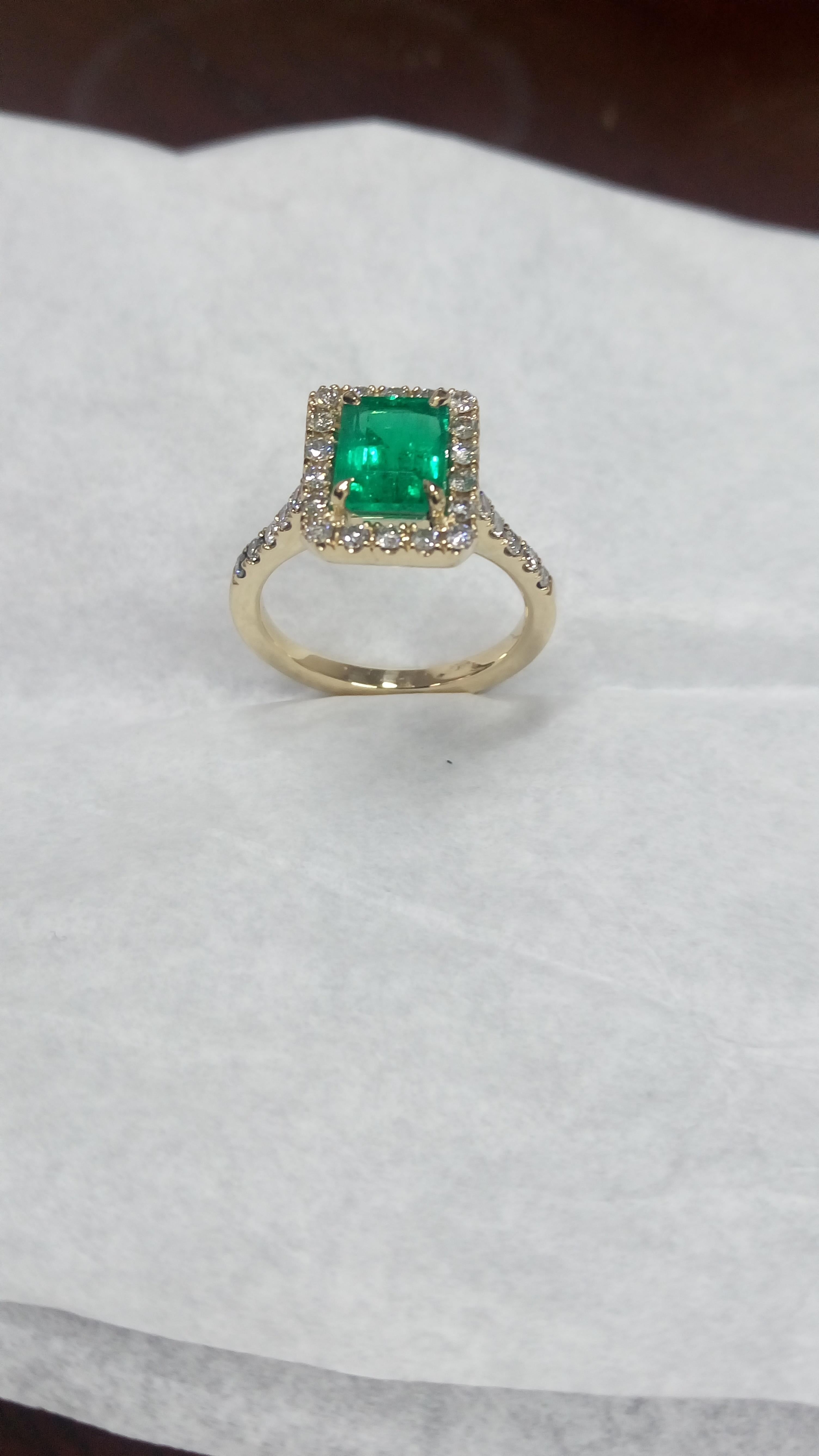 Colombian emerald and diamond engagement ring set in 18K yellow gold and surrounded by a diamond halo comprising 0.56 carats of diamonds.
