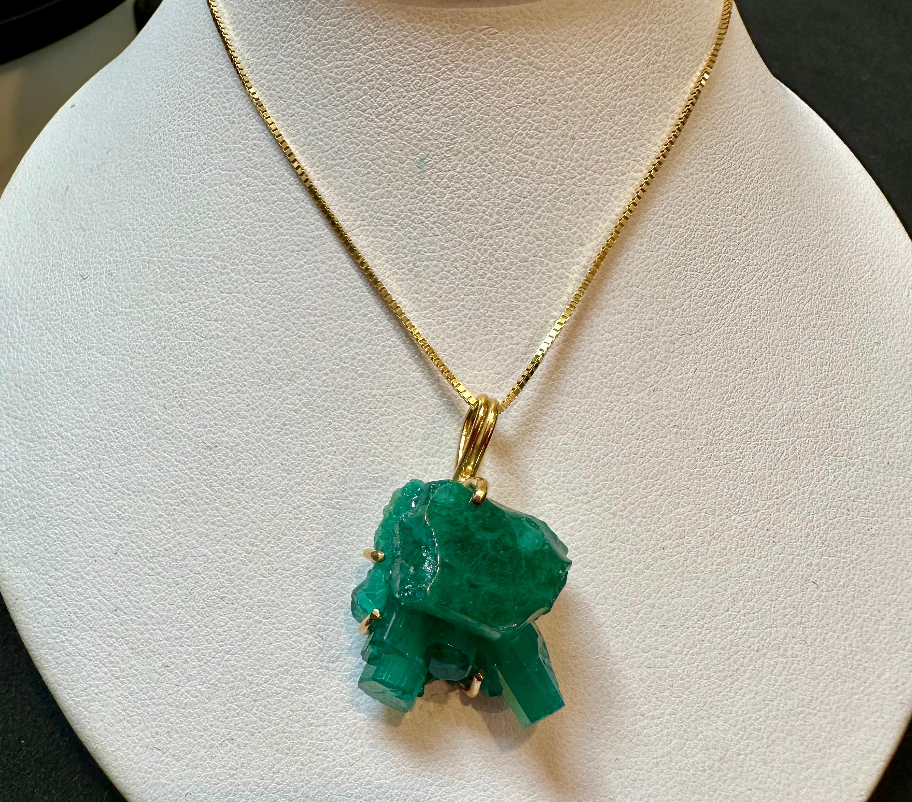 This Colombian Emerald Rough Pendant necklace is a breathtaking statement piece. It showcases a large, extremely fine 25 ct total weight emerald, beautifully set in 18 karat Yellow Gold. The pendant dangles from a scintillating bale and is