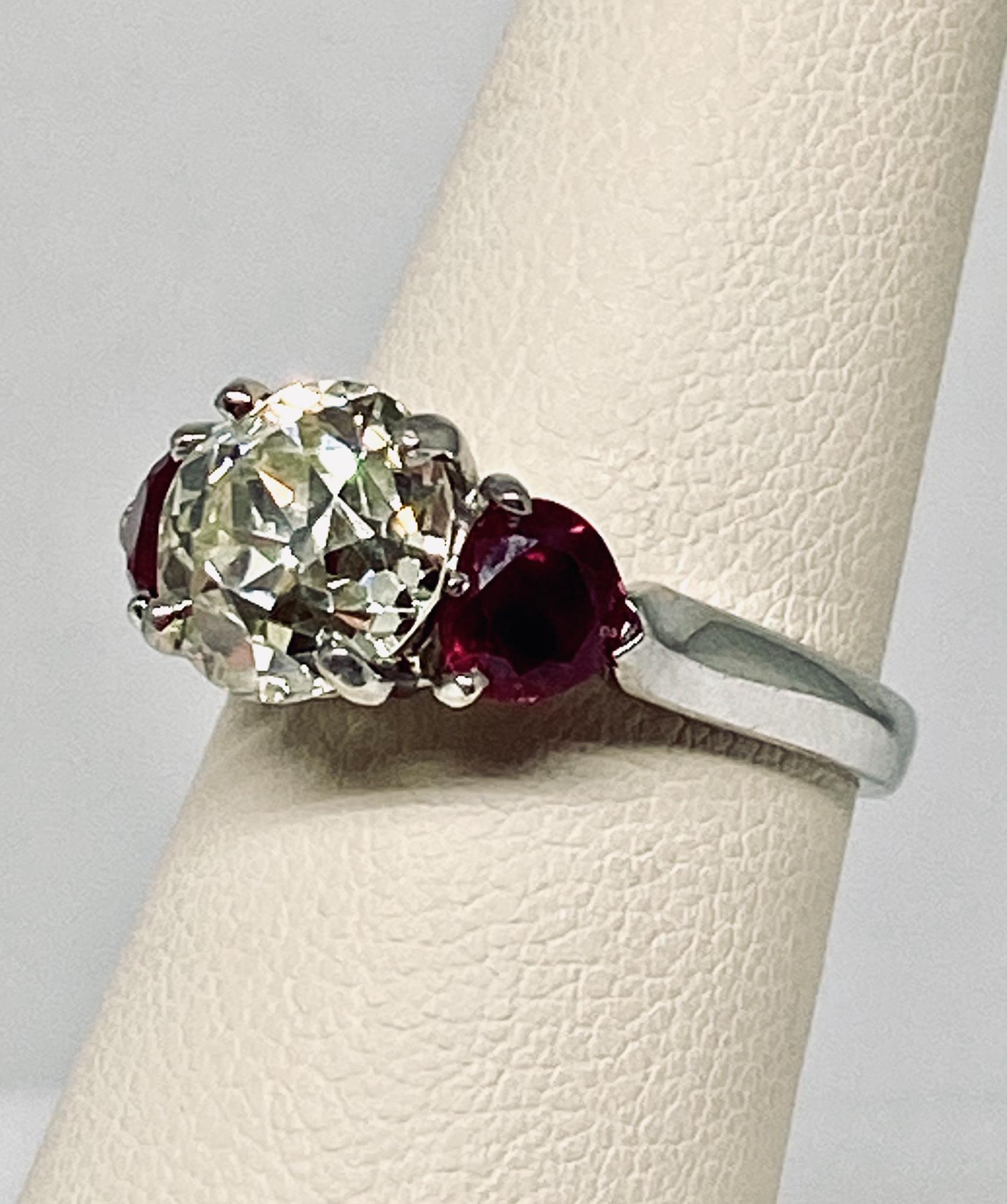 Beautiful estate 3 stone engagement style ring in platinum featuring a prong set round cut white diamond center stone weighing 2.50 carats with a K color grade and SI clarity flanked by two round cut prong set deep red rubies on a solid platinum