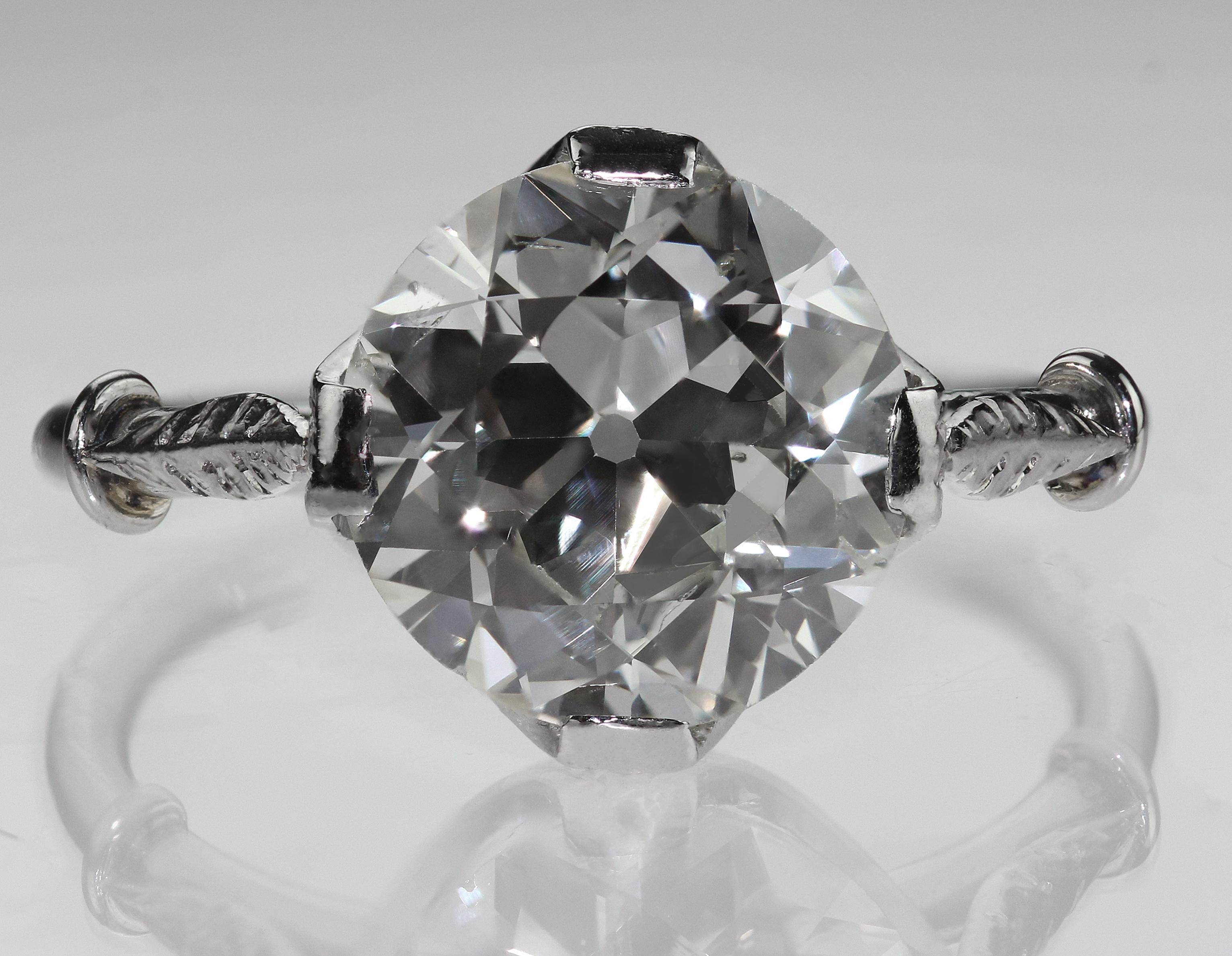 An Edwardian platinum single stone diamond ring featuring a dazzling Old European cut diamond that truly sparkles from every angle. This is a very fine antique example with detailed engravings on the stylised 'feather' shoulders and around the