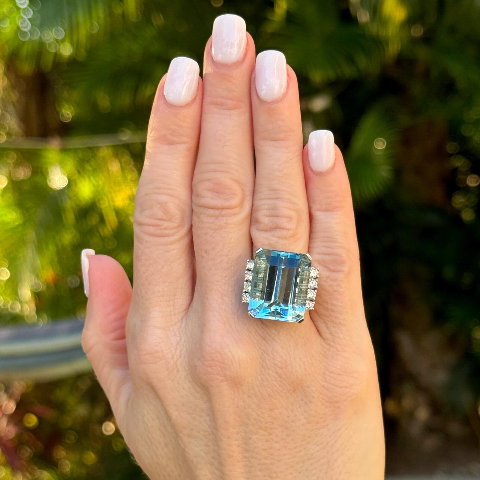 Stunning aquamarine diamond cocktail ring crafted in 18 karat white gold. The ring features an approximately 25 carat emerald cut aquamarine gemstone flanked by 8 round brilliant cut diamonds weighing approximately .88 CTW. The diamonds are graded