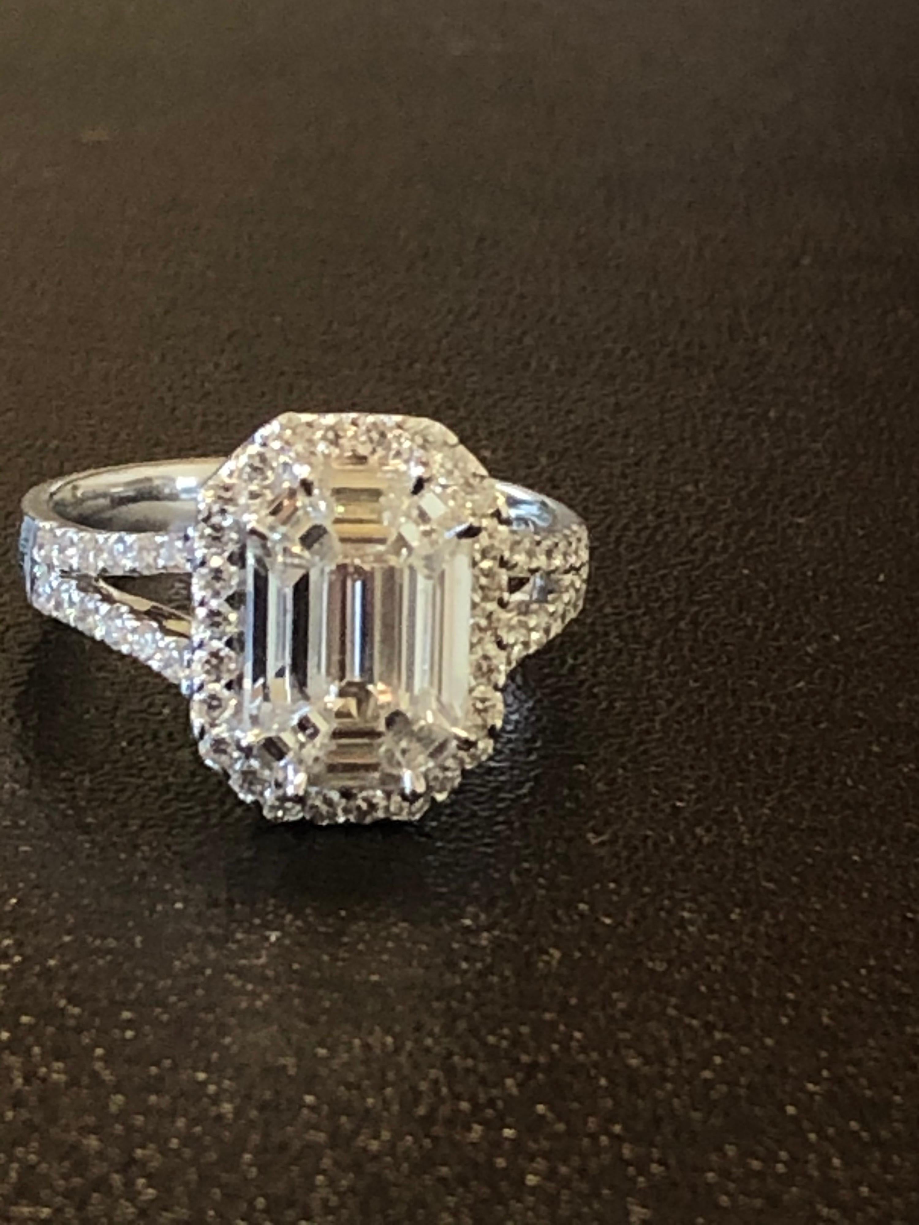 Baguette, Emerald, and Trapezoid shaped diamonds set in an illusion to create the look of a 6.50 to 7 carat single emerald cut stone. The ring is set with a halo of round diamonds and to the side of the ring. The ring is set in 18K white gold. The