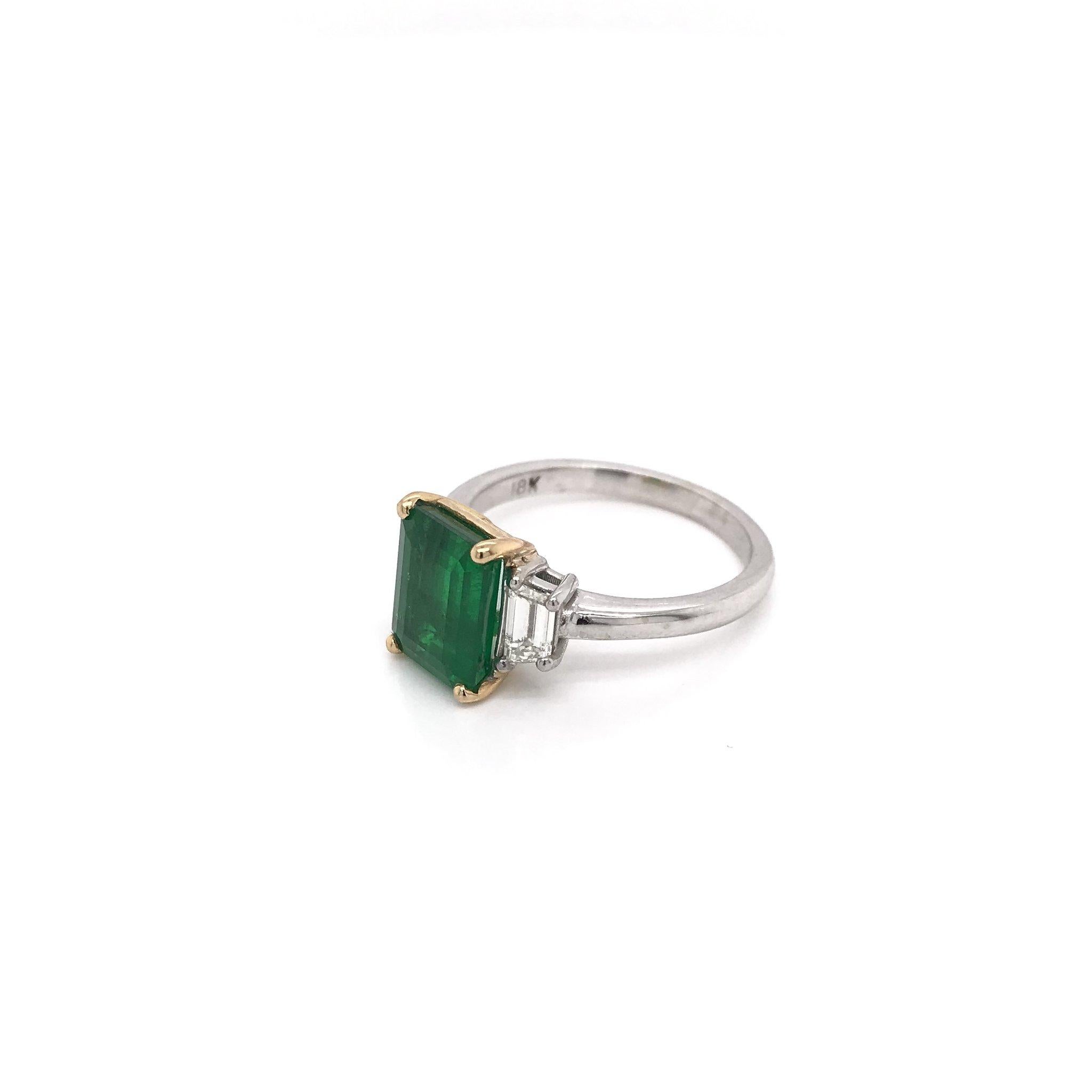 This modern classic is a contemporary piece. The center stone is a 2.50 carat natural emerald. The setting is 18k white gold with 18k yellow gold accents; a classic combination for fine emerald pieces. The setting features two trapezoid cut diamonds