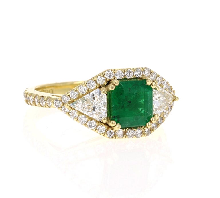 A gorgeous Emerald and Diamond Ring in a classic halo setting and resembling a three-stone ring! This gorgeous Emerald is natural and weighs 1.32 Carats.  It measures at 6.5 mm x 6.5 mm.
It has 46 Round Cut Diamonds that weigh 0.56 carats and 2