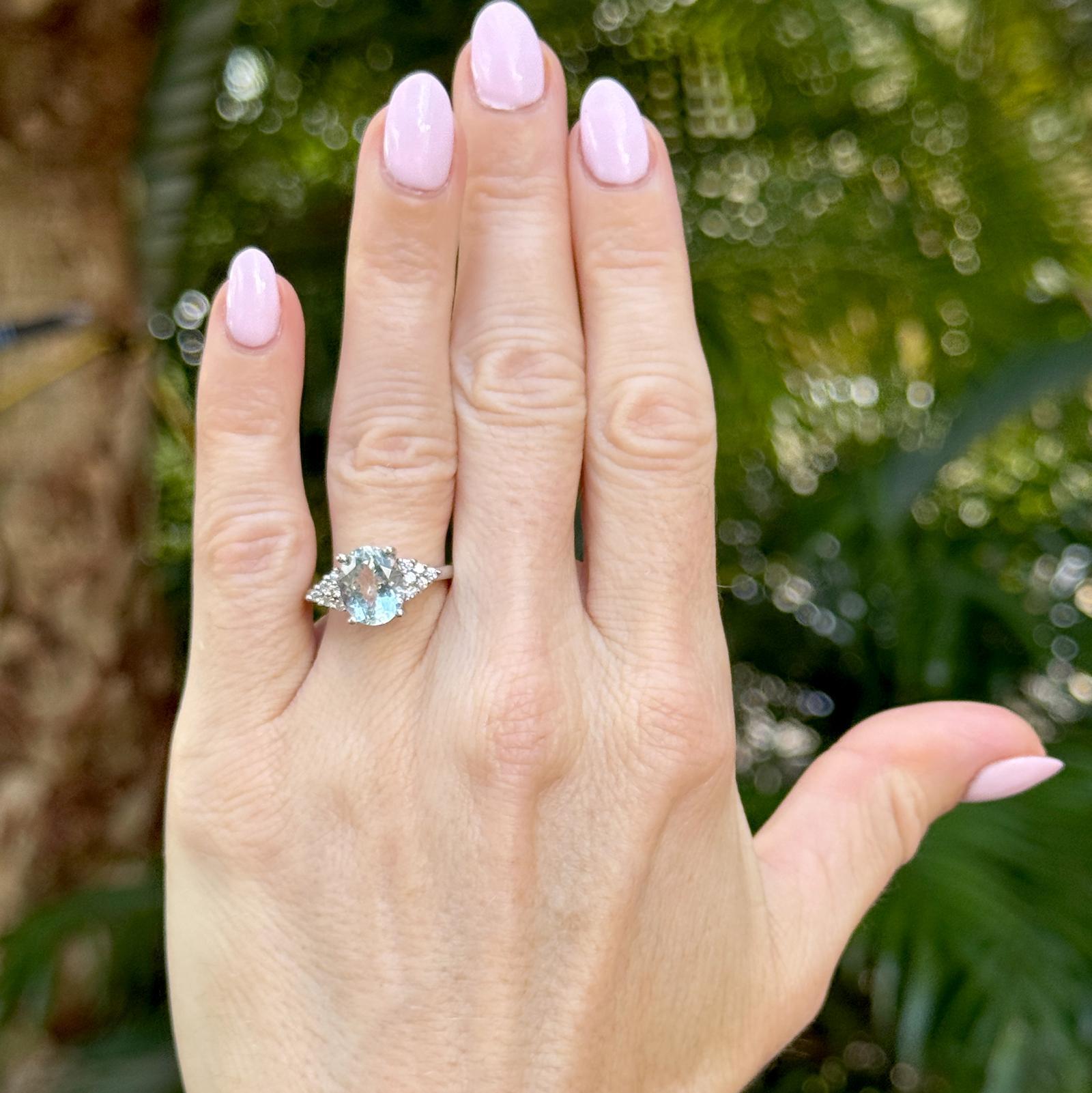 Dieser elegante Ring aus 14-karätigem Weißgold präsentiert einen atemberaubenden ovalen Aquamarin von etwa 2,50 Karat, der in einem ruhigen, eisblauen Farbton erstrahlt. Der Aquamarin wird von 12 runden Diamanten im Brillantschliff flankiert, die in