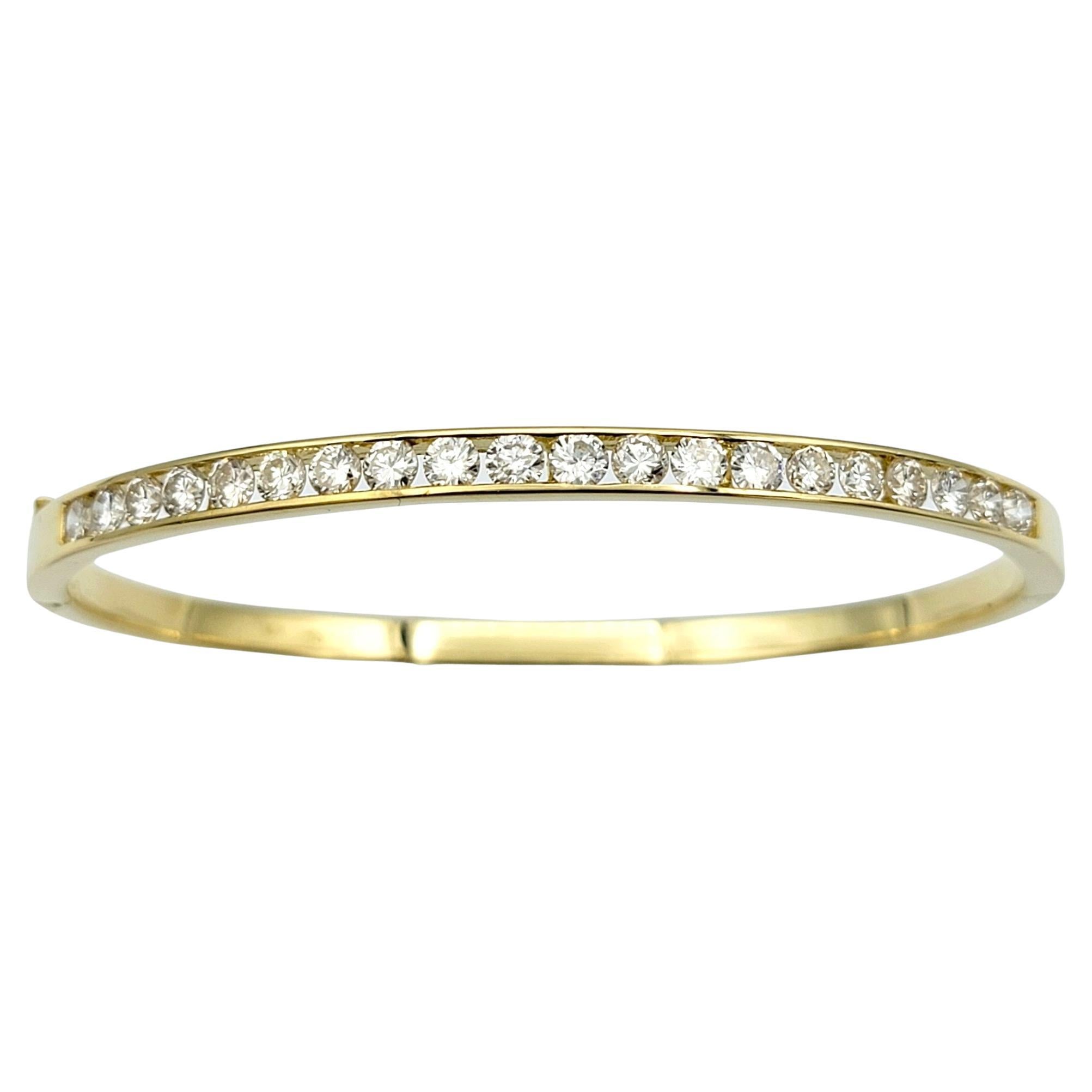 This breathtaking diamond hinged bangle bracelet exudes sophistication and luxury with its sleek design and brilliant sparkle. Crafted from lustrous 18 karat yellow gold, the bangle features a row of 20 dazzling round diamonds securely nestled