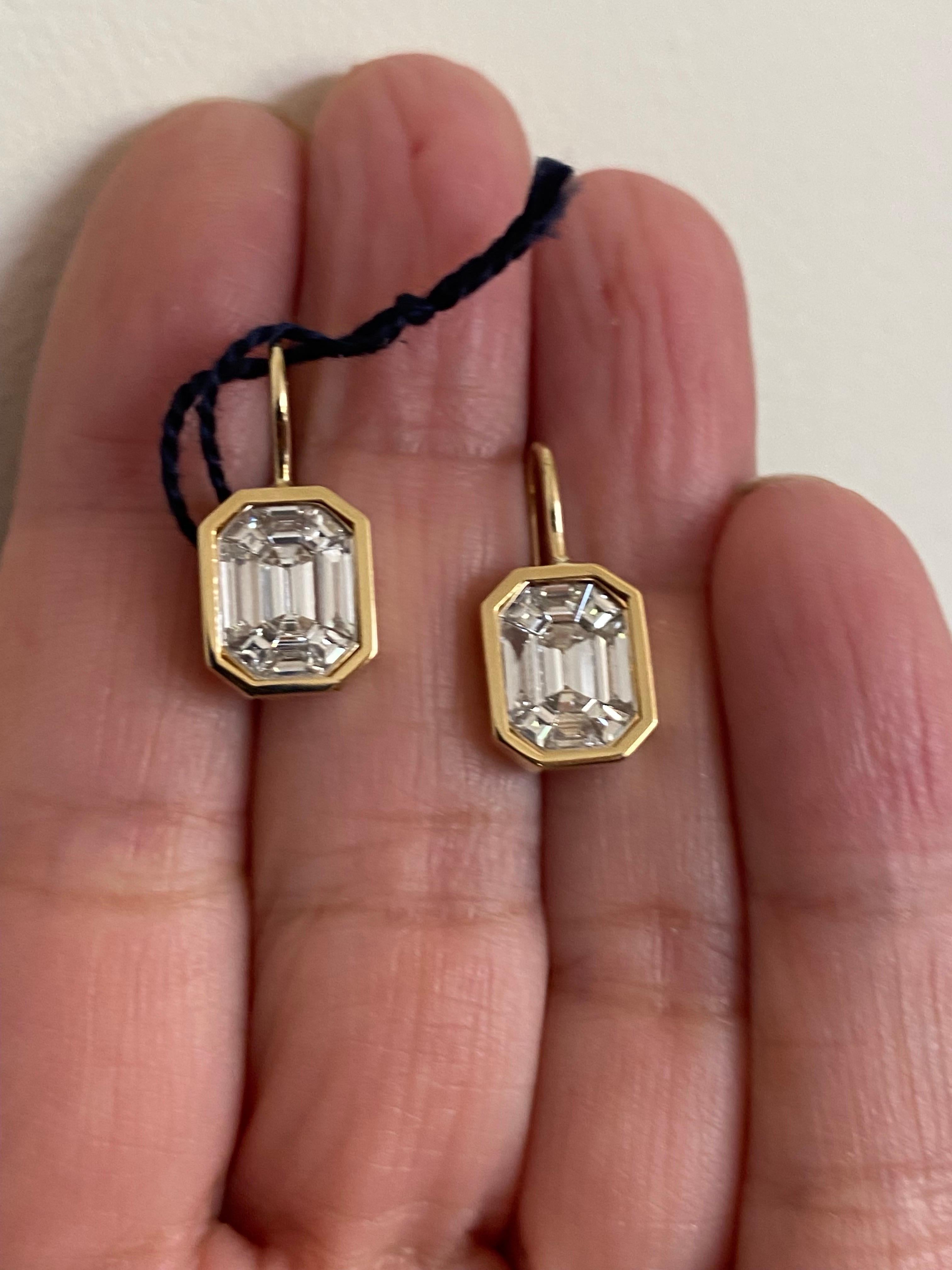 Hanging emerald cut illusion earrings on bezel set in 18K yellow gold. The earrings are a composite of baguette and trapezoid diamonds to create the illusion of a single emerald cut stone. The color of the stones are F and the carat weight is VS1.