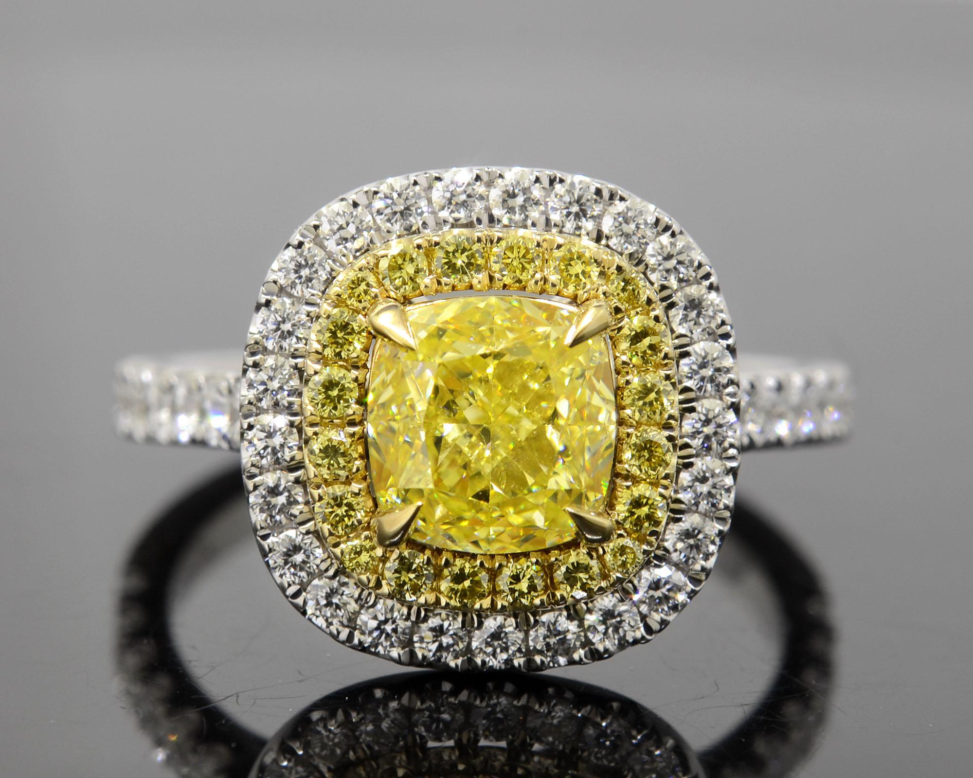 This lovely double halo Fancy Yellow Diamond Ring features a 1.50 Ct. natural fancy yellow cushion cut diamond with VS2 clarity. Surrounding the center gem and the shank are 1.00 Ct. of round cut fancy yellow and white diamonds in U-Pave setting.