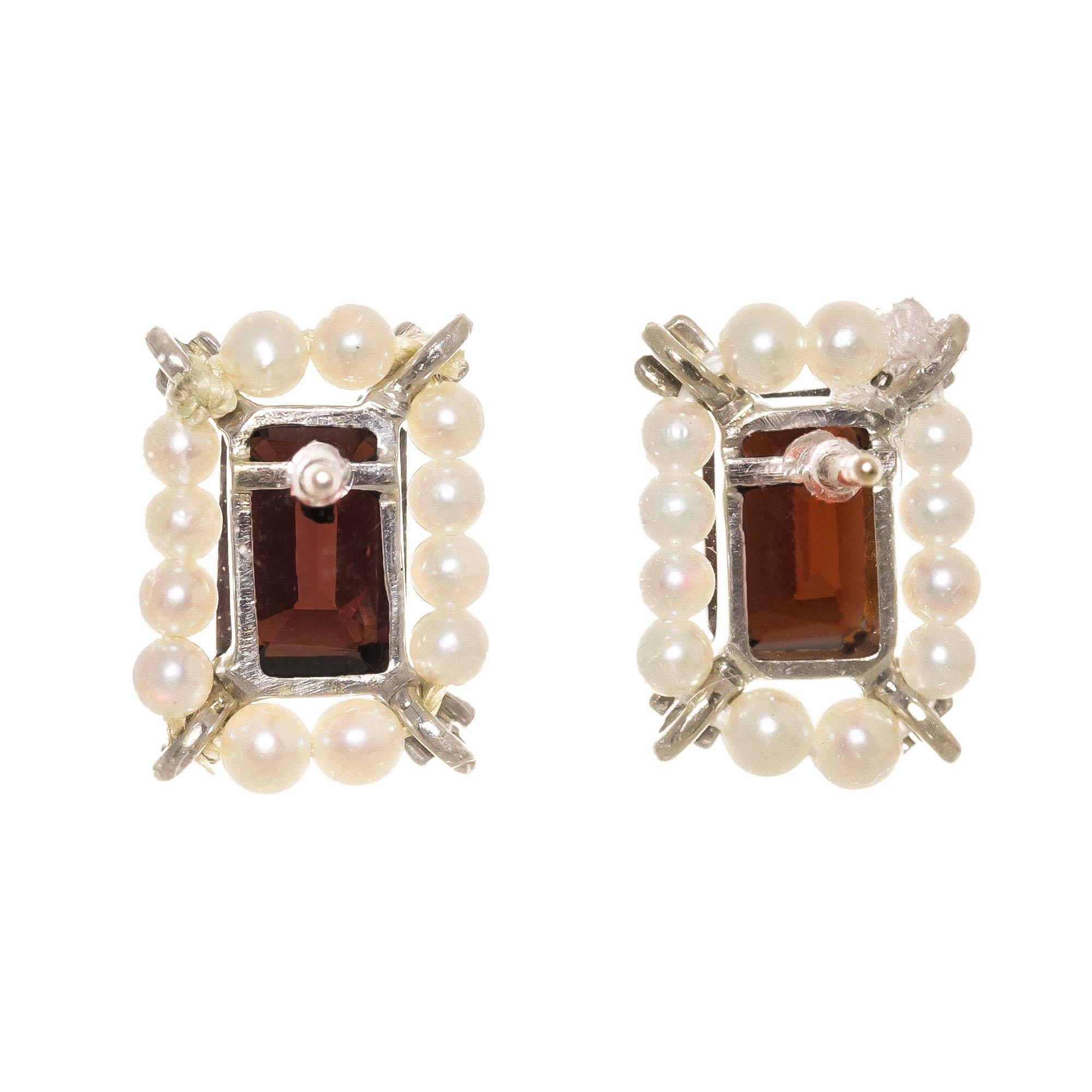 Emerald cut garnet center stones with a halo of cultured pearls in a simple 14k white gold settings. 

2 rectangular brownish red garnets, approx. 2.50cts
24 cultured white pearls, 2.5mm
14k white gold 
Stamped: 14k
2.4 grams
Top to bottom: 12.1mm