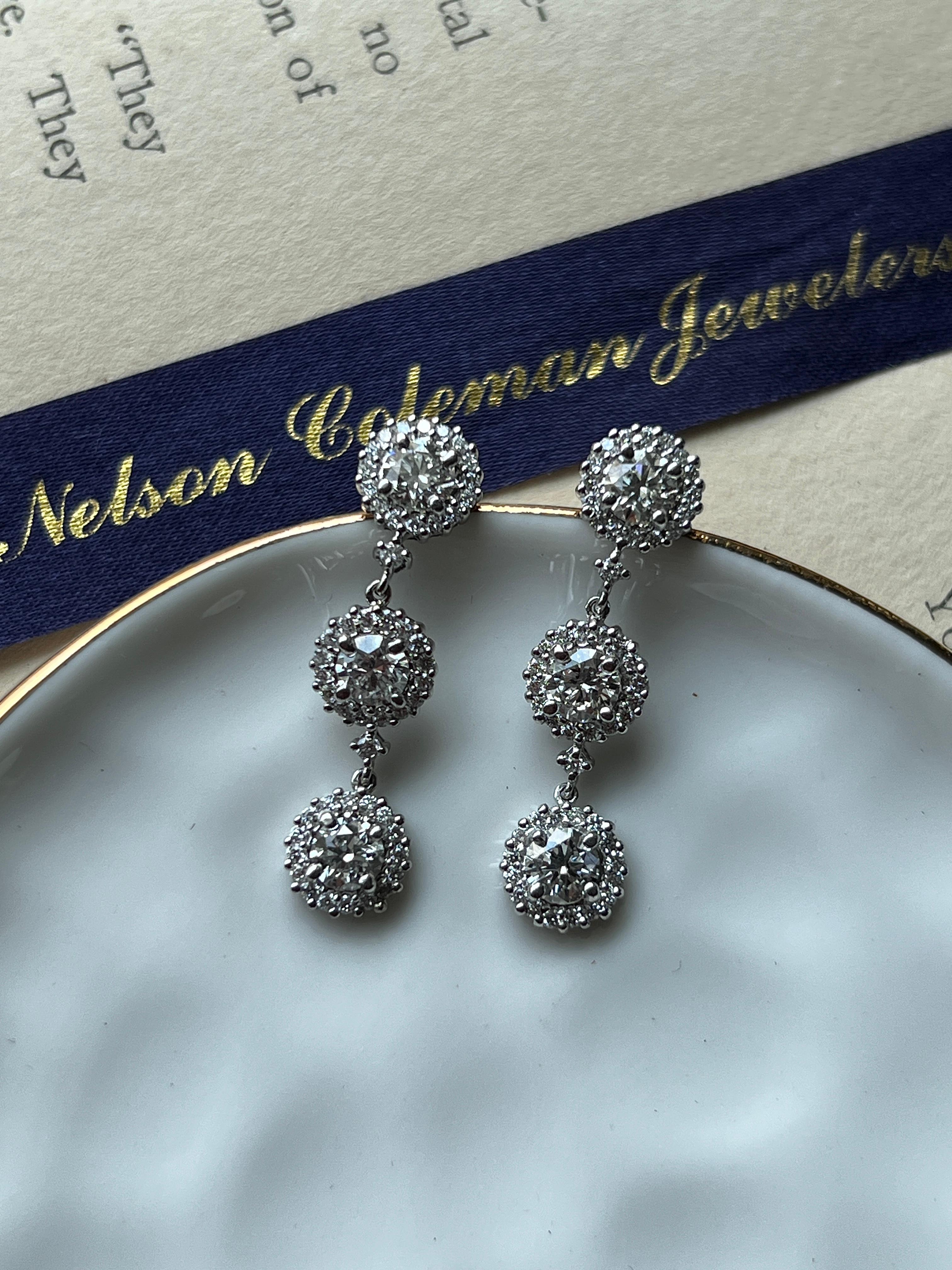 One pair of contemporary 14 karat white gold diamond cluster drop earrings, designed with elegant movement and brilliant sparkle. Each earring is composed of three larger diamonds with a halo around it. The earrings combined have six larger round