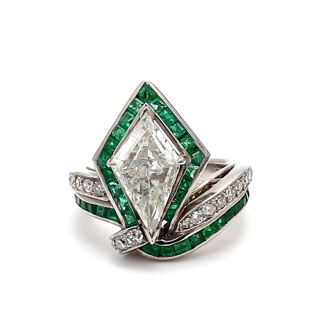 Titre :
Cette bague Art déco en platine présente un diamant en forme de cerf-volant de 2,14 carats, de couleur H et de pureté I1, serti dans un cadre géométrique audacieux d'émeraudes taille carré d'une valeur totale de 1,50 carat. Le design